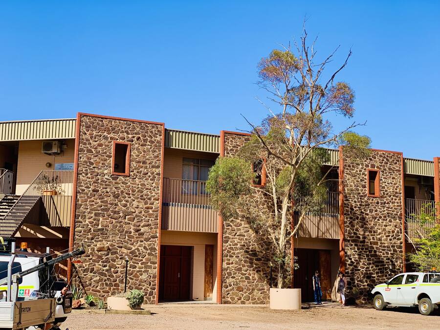 A building with stone walls and multiple balconies, a staircase, and a vehicle parked in front.