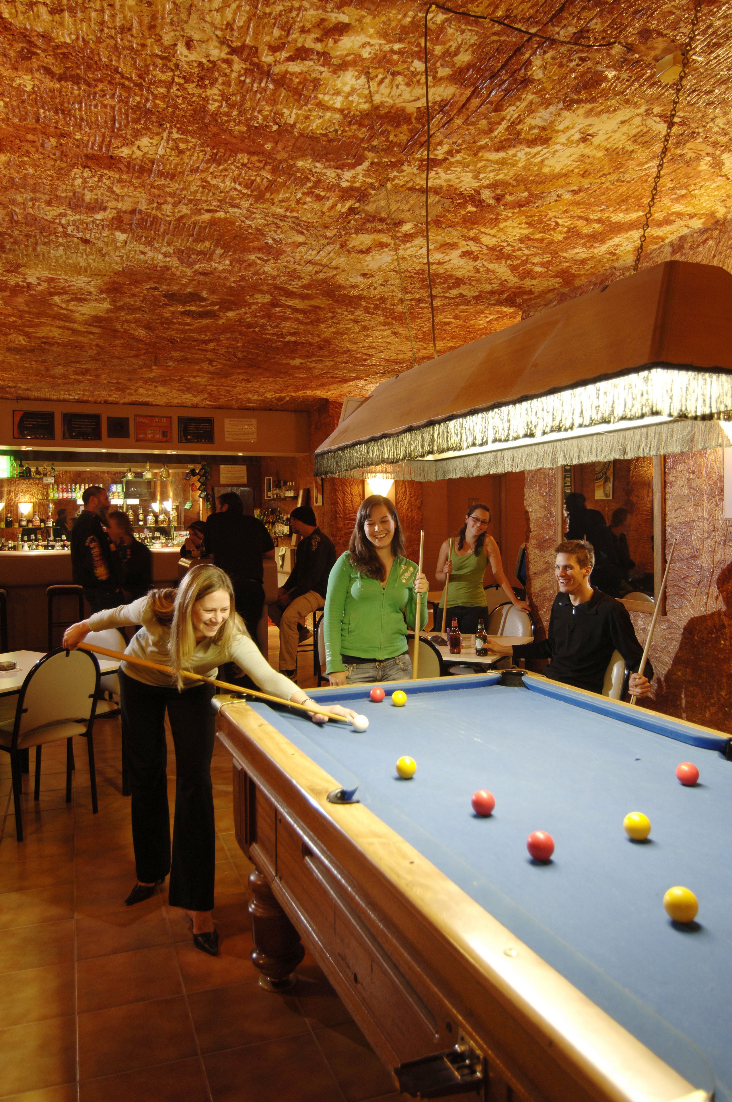 Una mesa de billar en una habitación con techo estampado y una zona de bar al fondo.