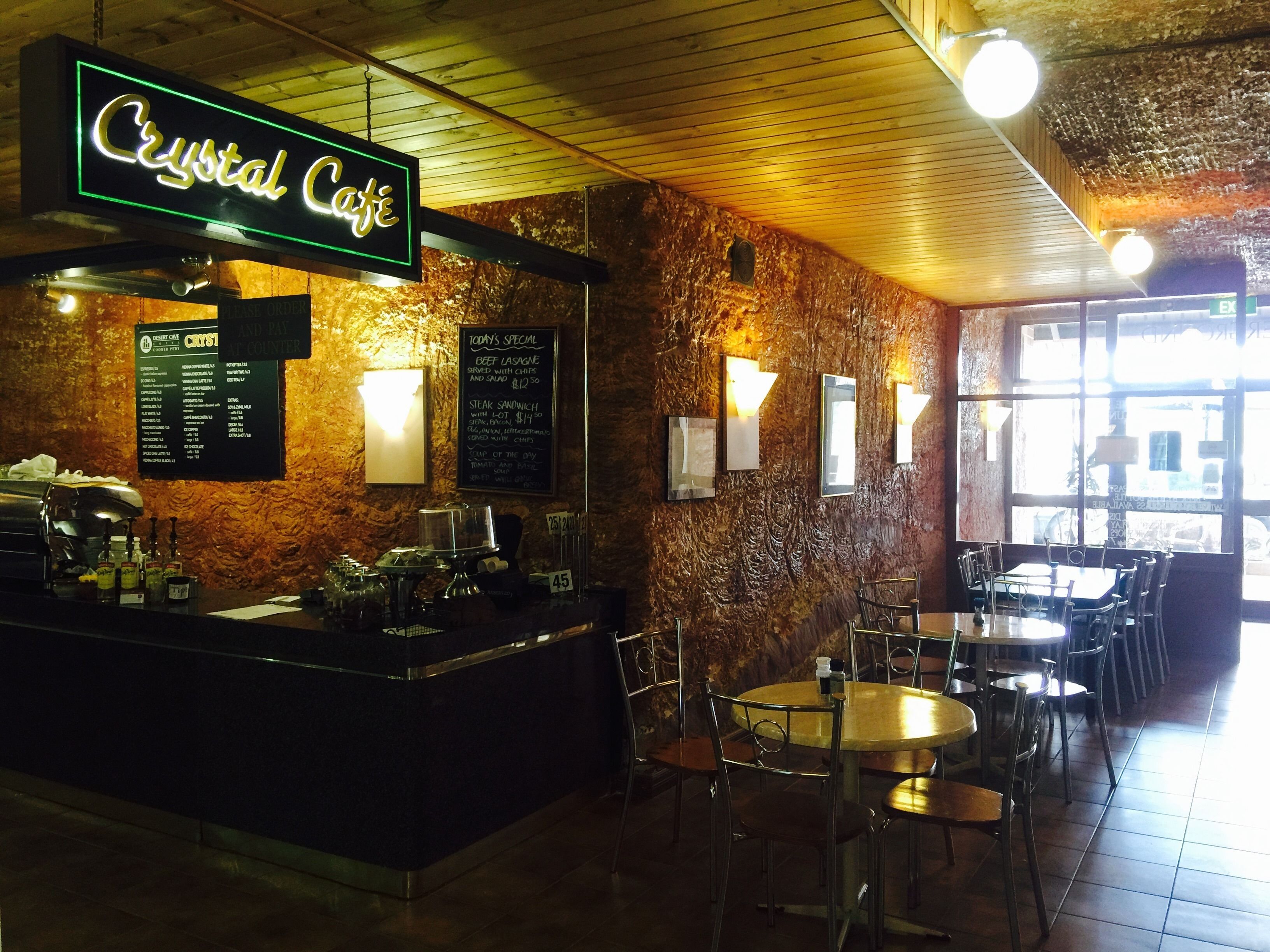 A restaurant interior with a neon sign reading "Crystal Cafe," a menu board, and a bar area.