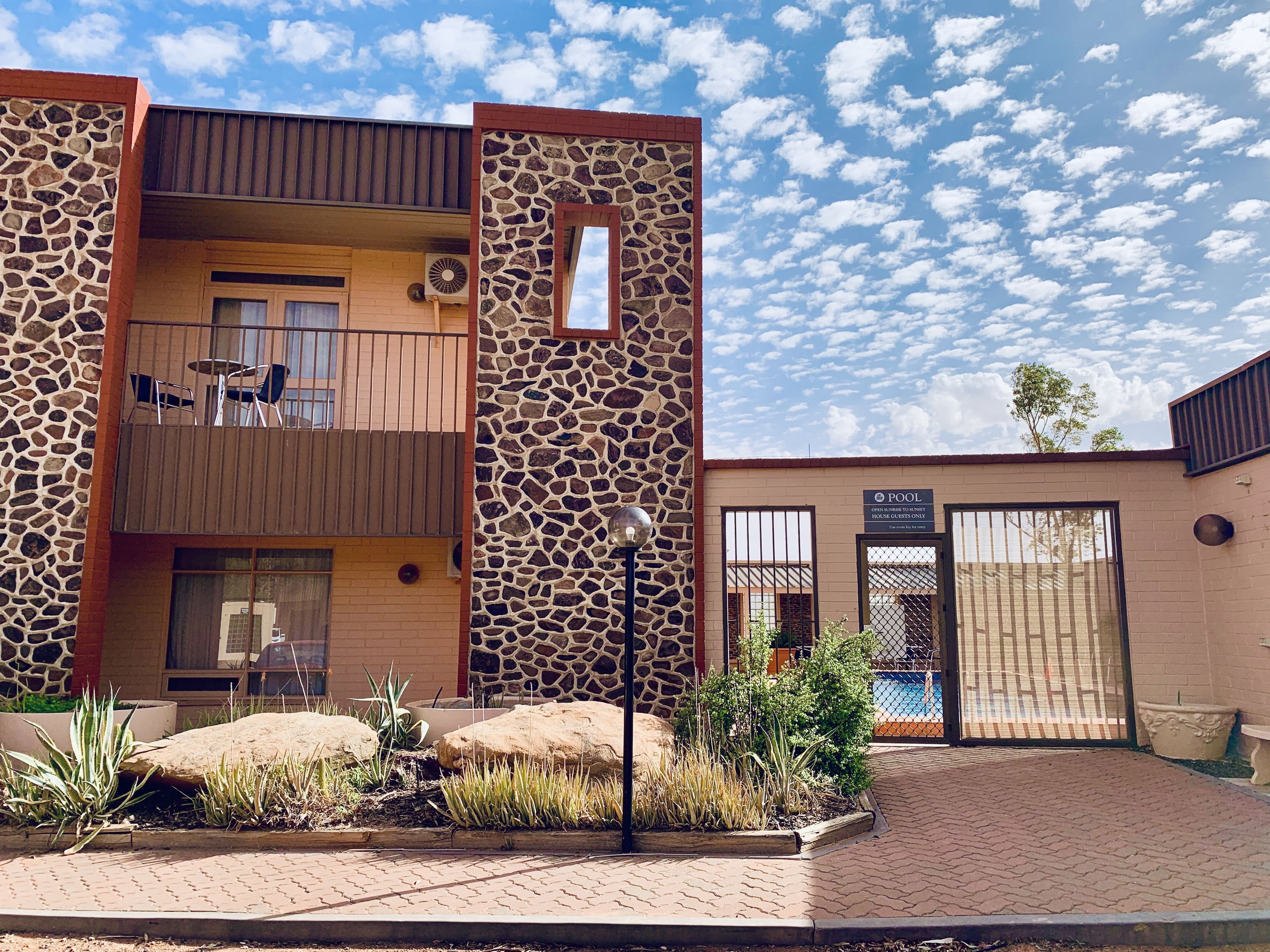 A modern building with a stone facade, a balcony with chairs, and a sign indicating it's a pool house.