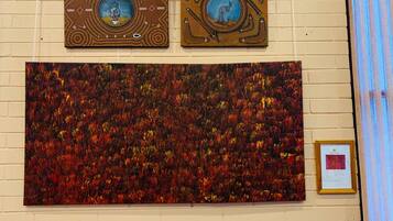 Een muur met drie kunstwerken: twee ingelijste schilderijen met Aboriginal designs en een groot abstract schilderij.