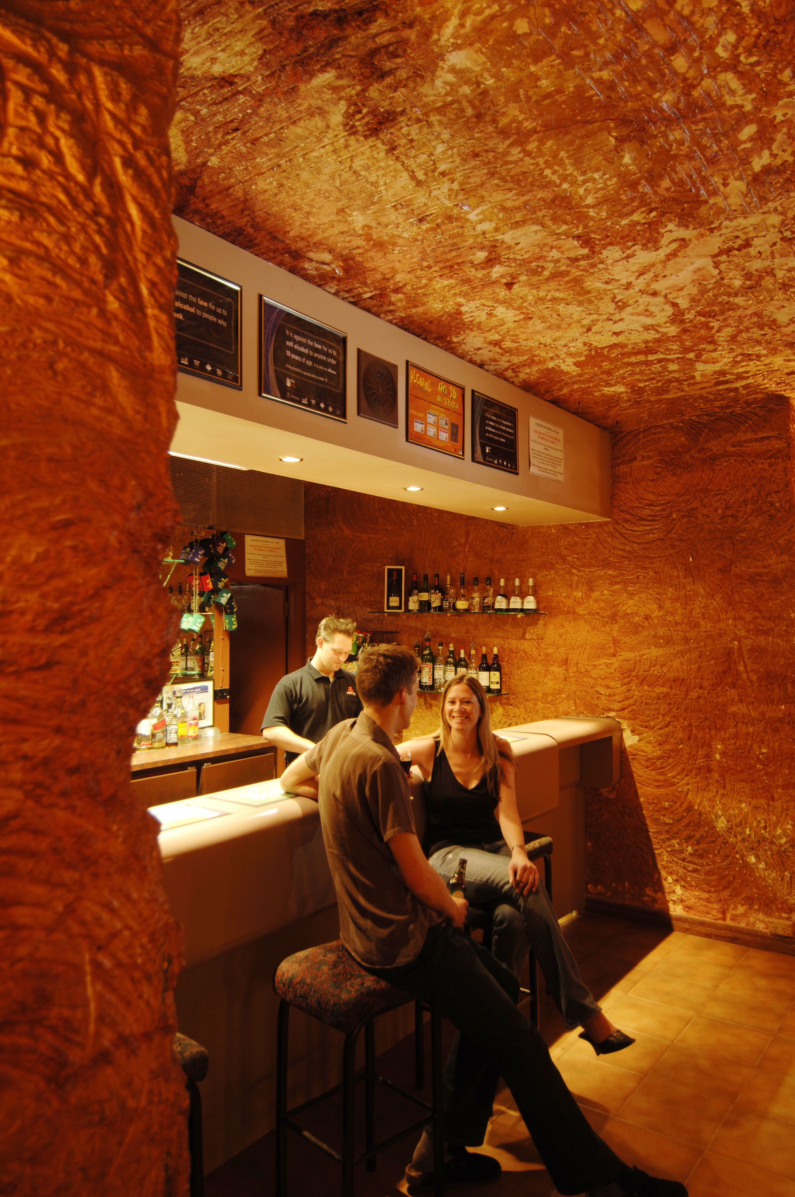 A bar area with a rustic wooden ceiling, a bartender, and a customer seated at the bar.