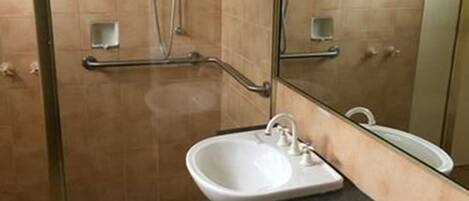 A bathroom with a glass shower enclosure, a sink, and a large mirror.