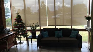 A living room with a sofa, a small table, a Christmas tree, and a large window with blinds.