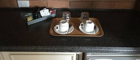 Eine Küchenzeile mit zwei weißen Kaffeetassen auf Untertassen, einer Tablett mit Gewürzen und einer Backsteinwand im Hintergrund.