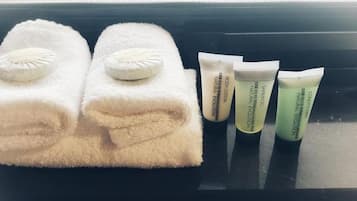 Un plateau noir avec deux serviettes blanches et trois tubes de lotion pour le corps, posés sur un rebord de fenêtre.