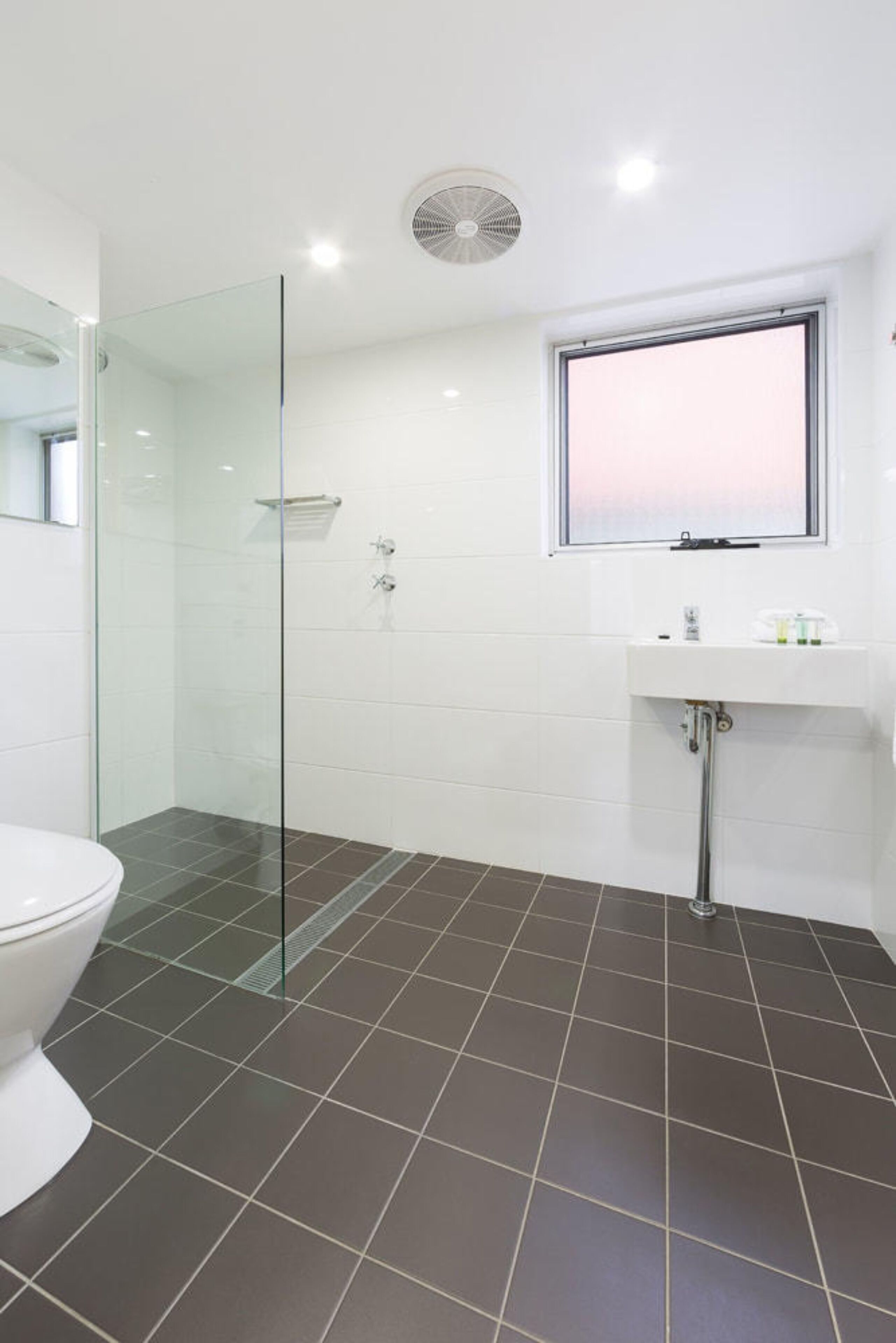 A bathroom with a glass-enclosed shower, a white toilet, and a sink with a window above it.