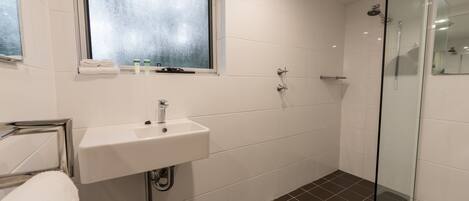 A bathroom with a white sink, a glass shower enclosure, and a window with frosted glass.