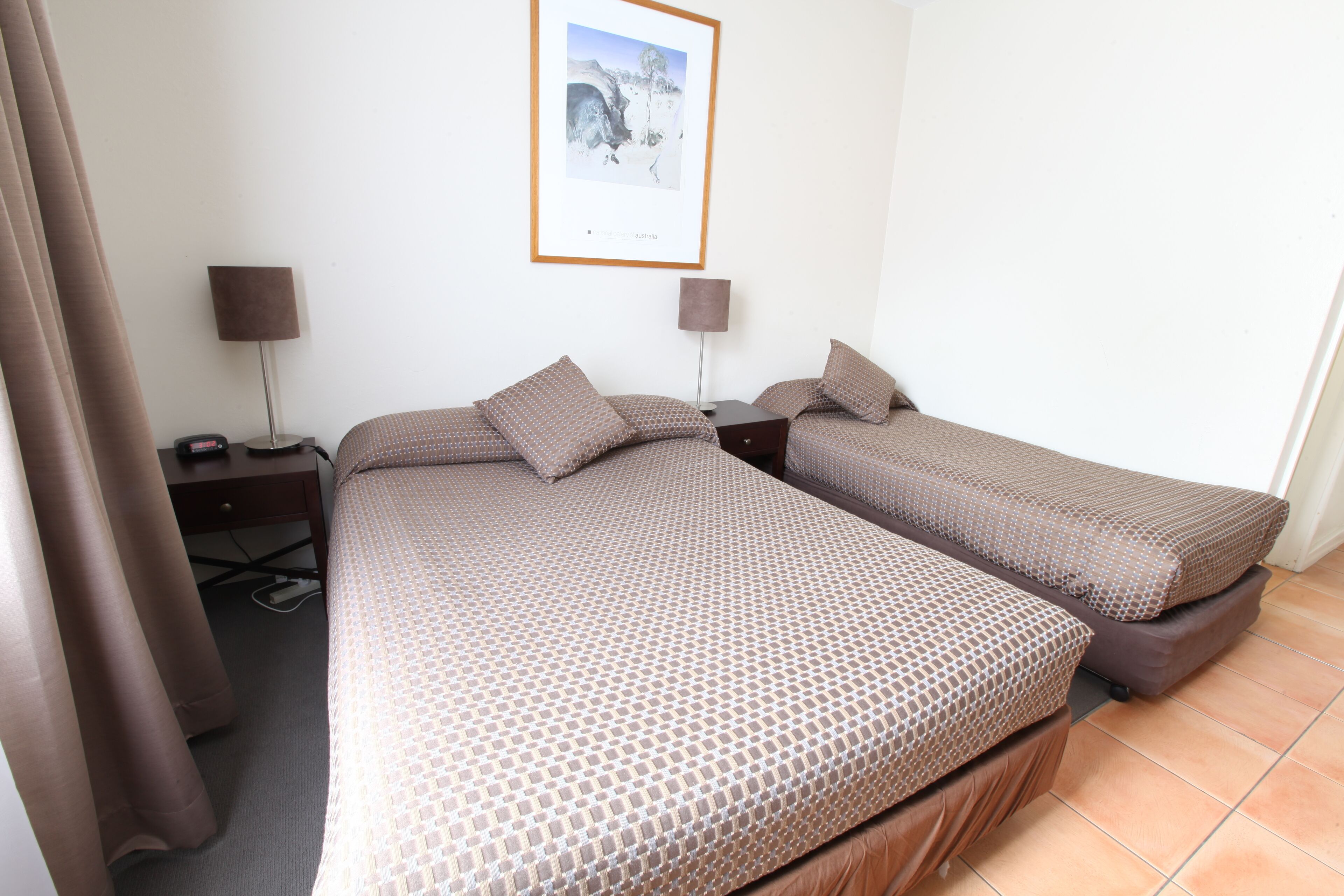 Habitación de hotel con dos camas, un escritorio, una silla, una lámpara y un cuadro en la pared.