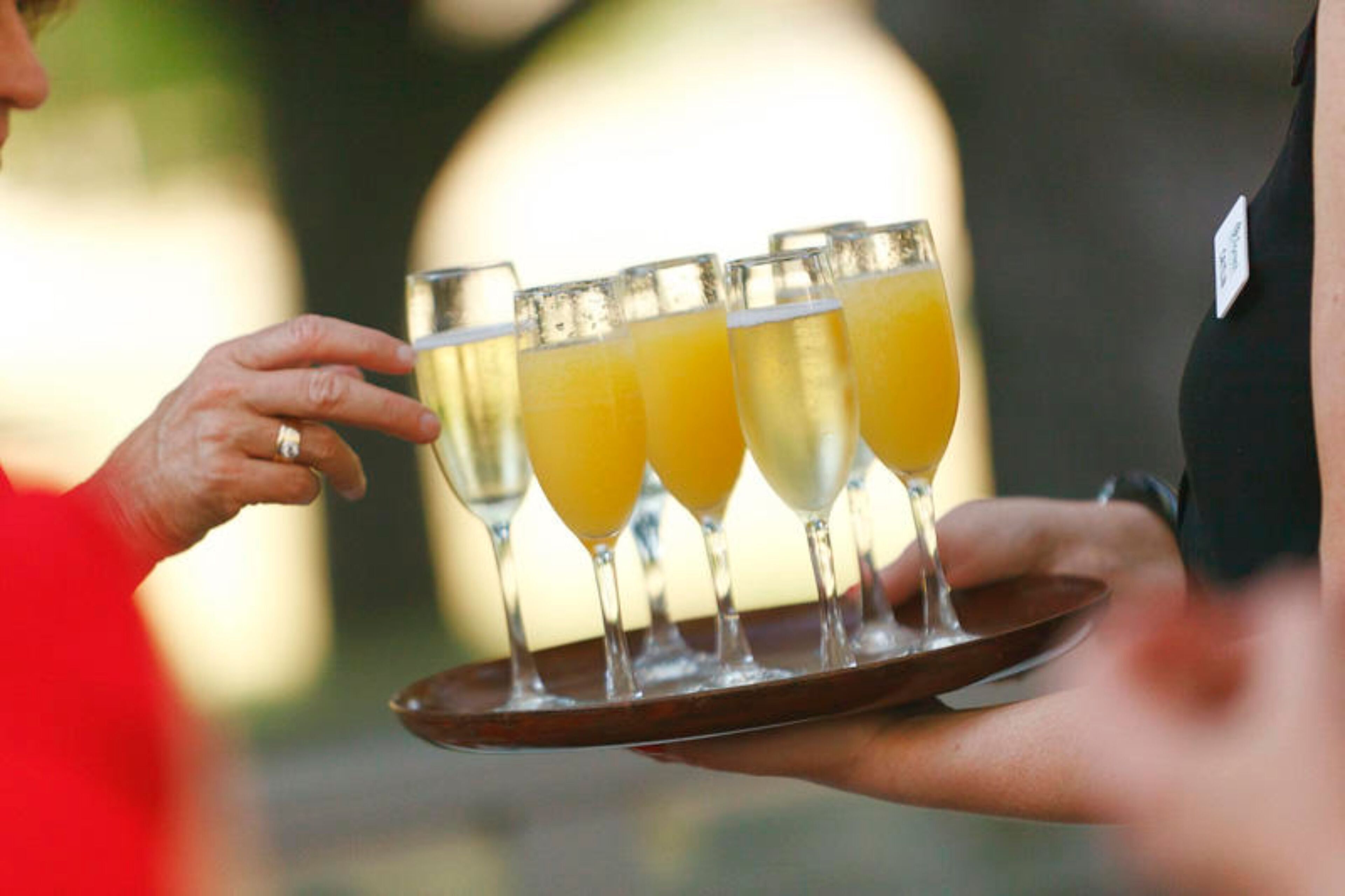 Une personne tenant un plateau sur lequel se trouvent quatre verres de jus d’orange.
