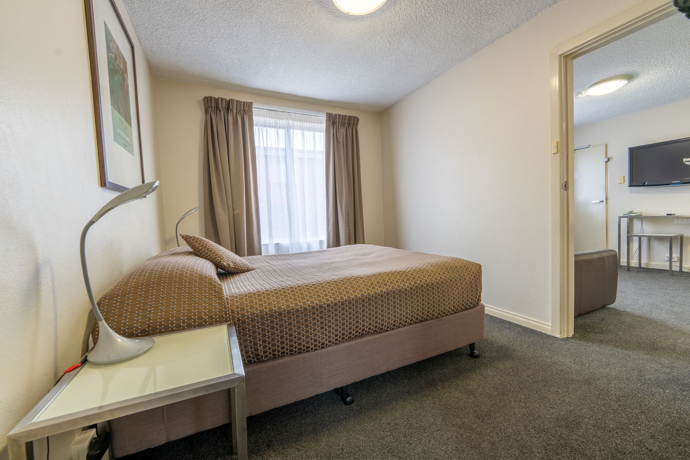 A hotel room with a single bed, a desk with a lamp, a television, and a window with curtains.