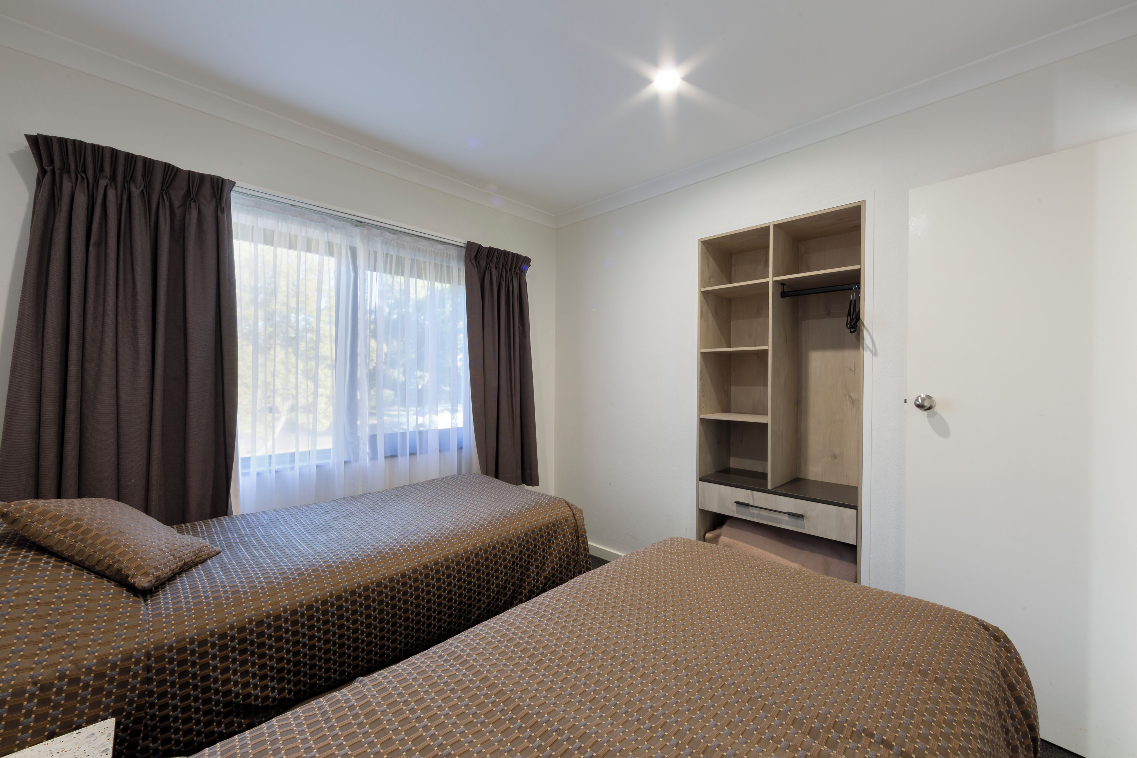 A bedroom with two beds, a wardrobe, and a window with curtains.