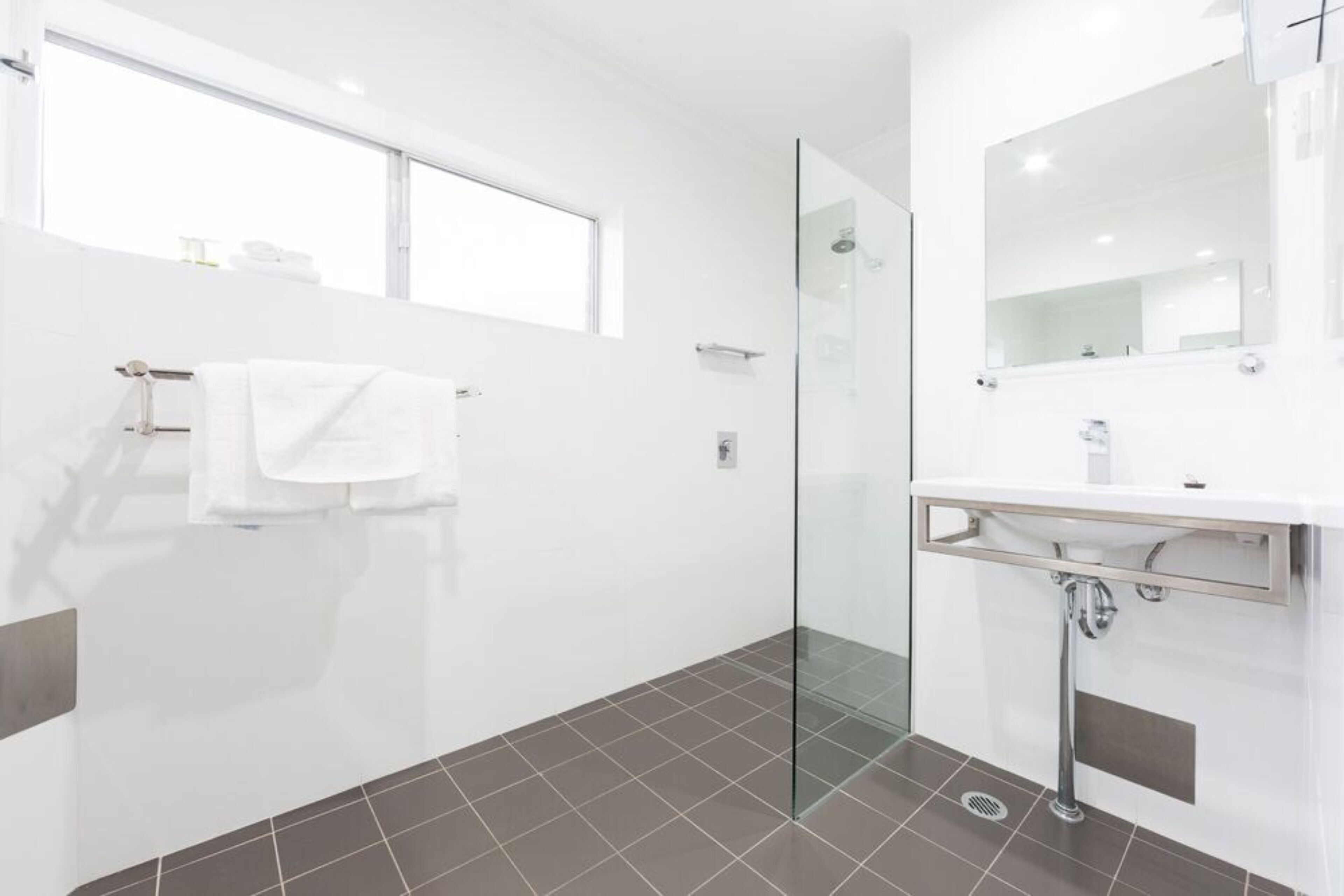 A modern bathroom with a glass shower enclosure, a white sink, and a large mirror.