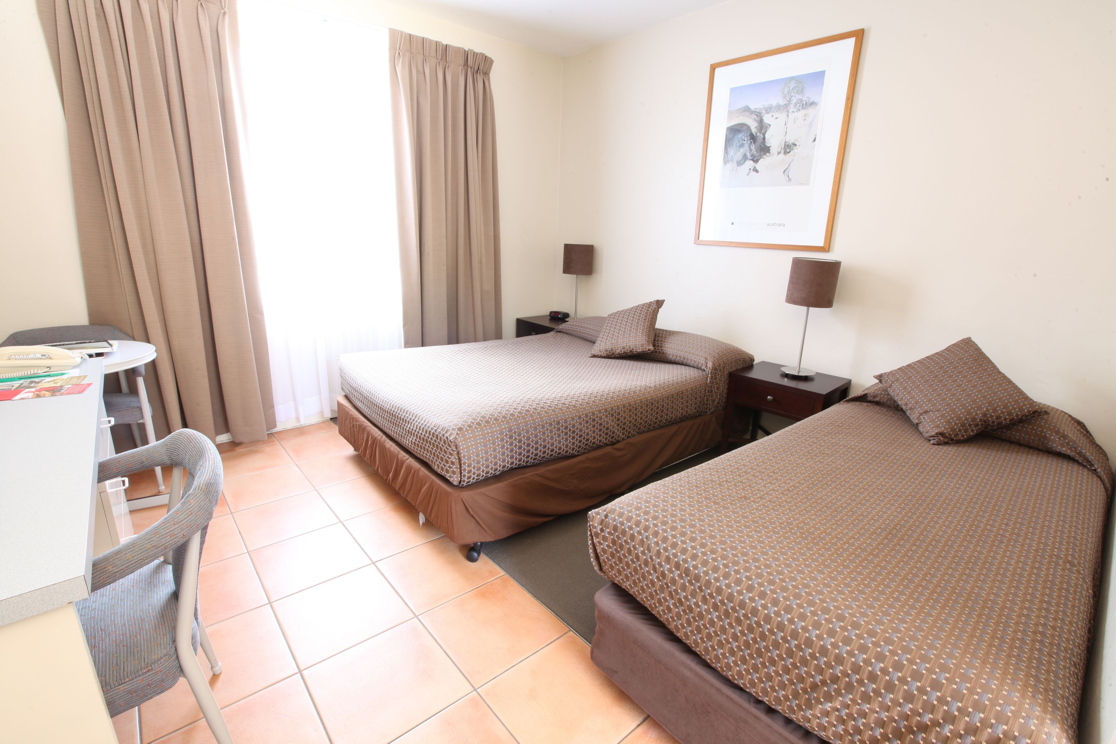 A hotel room with two beds, a desk, and a chair.
