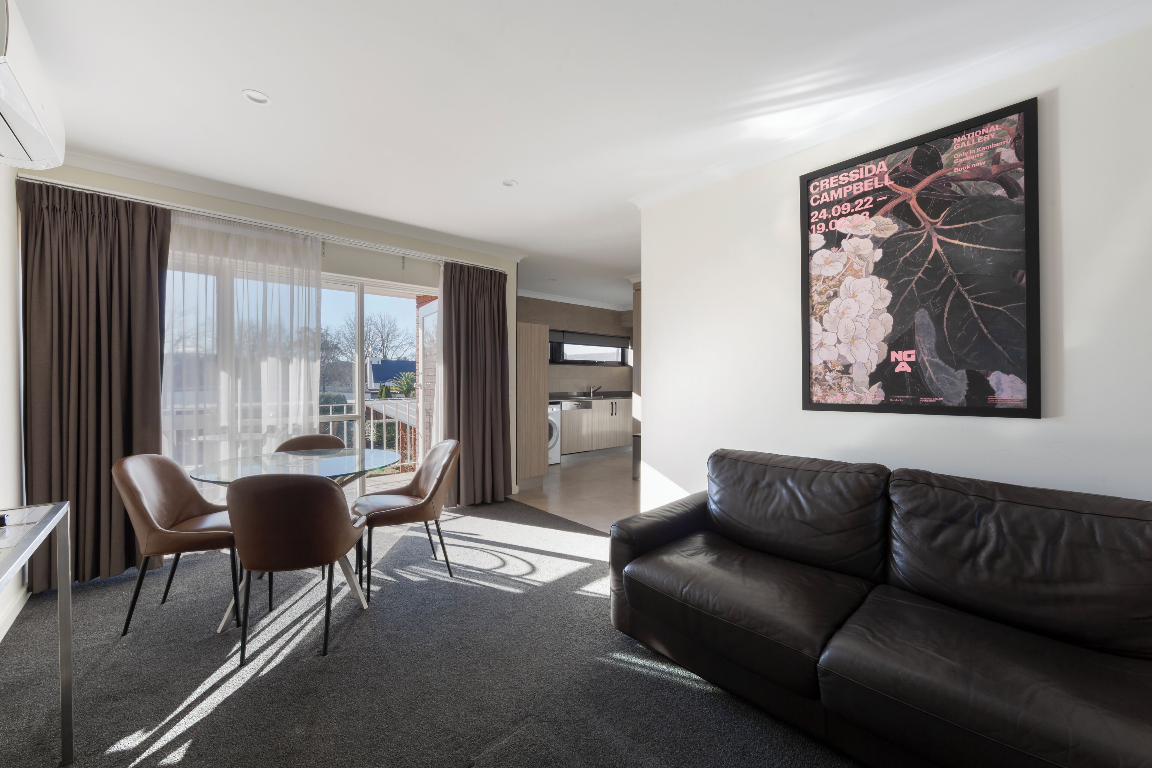 A modern hotel room with a dining area, a sofa, and a kitchen in the background.