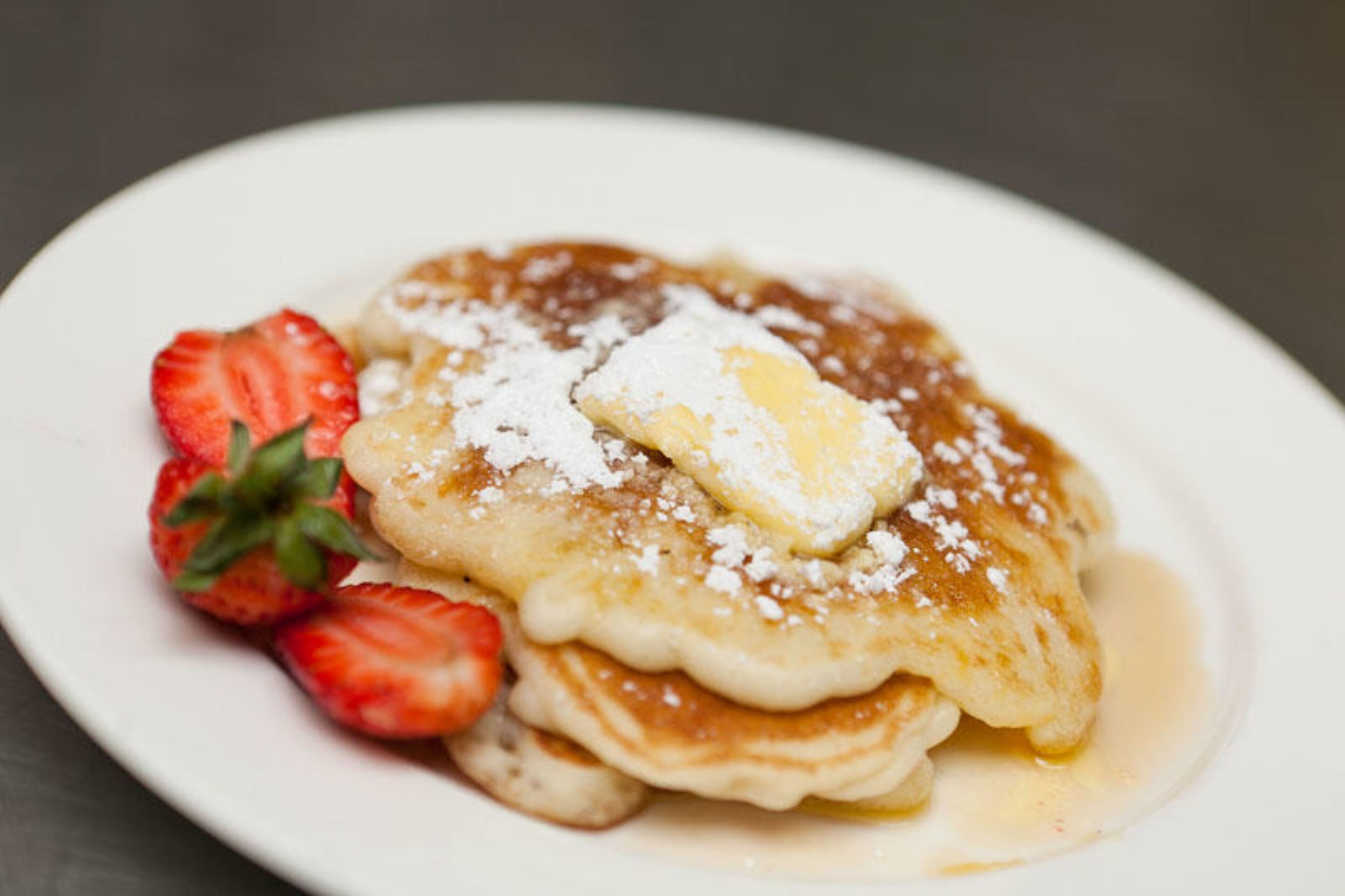 A plate of pancakes with strawberries and a pat of butter.
