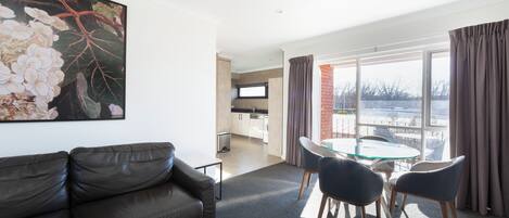 A modern living room with a leather sofa, a glass table with chairs, and a large window with curtains.