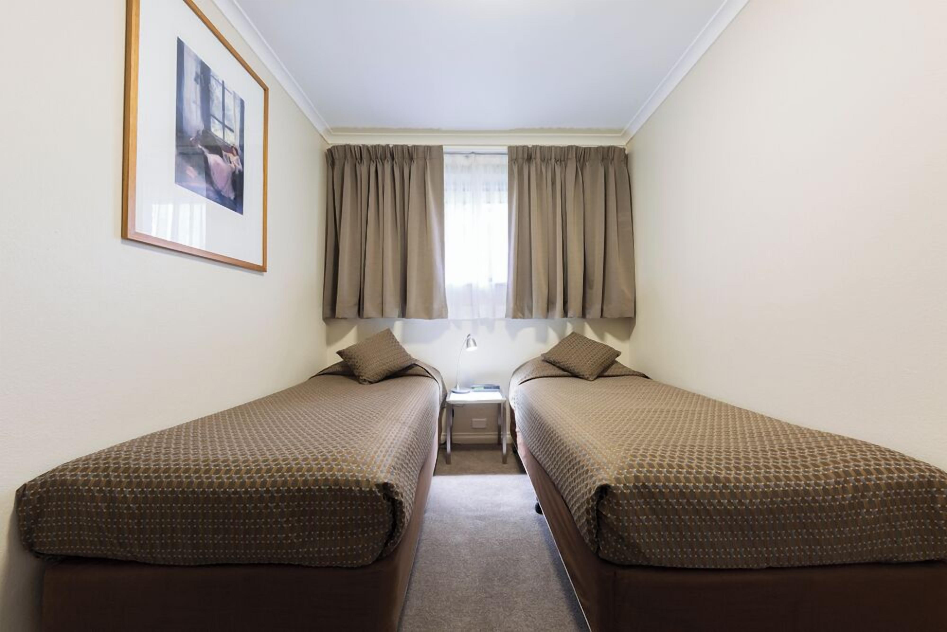 A small, clean room with two single beds, a framed picture on the wall, and a window with curtains.