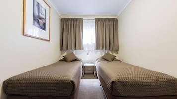 A small, clean room with two single beds, a framed picture on the wall, and a window with curtains.