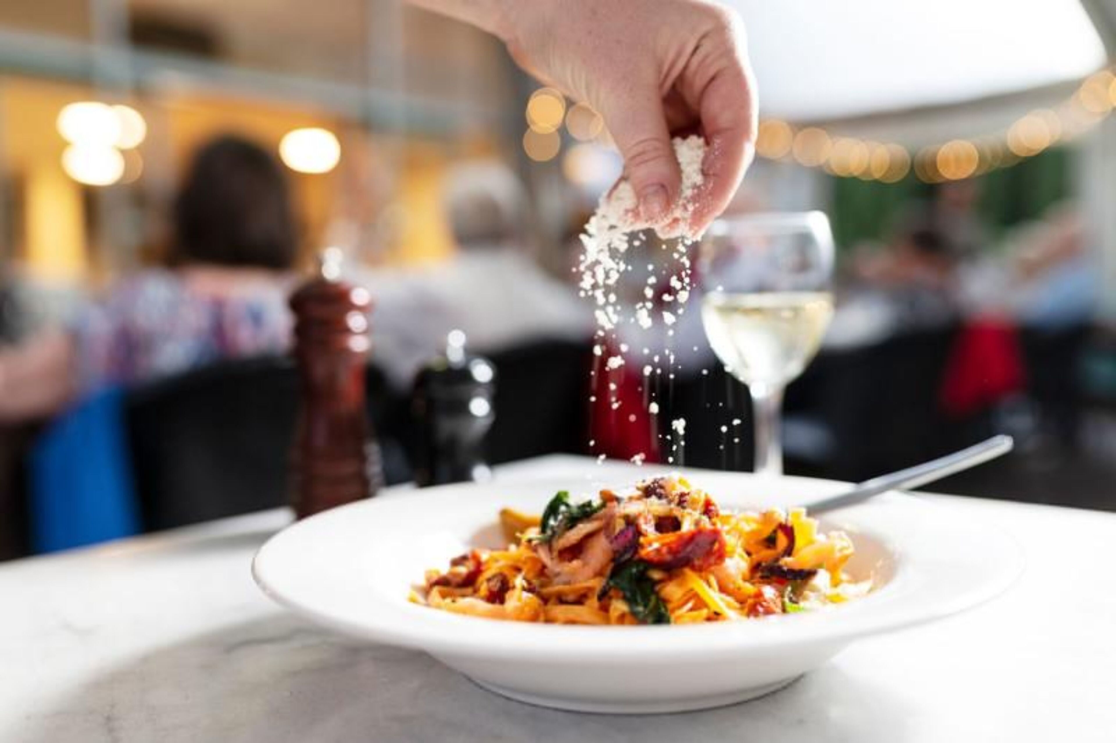 A hand sprinkling seasoning over a dish of pasta.