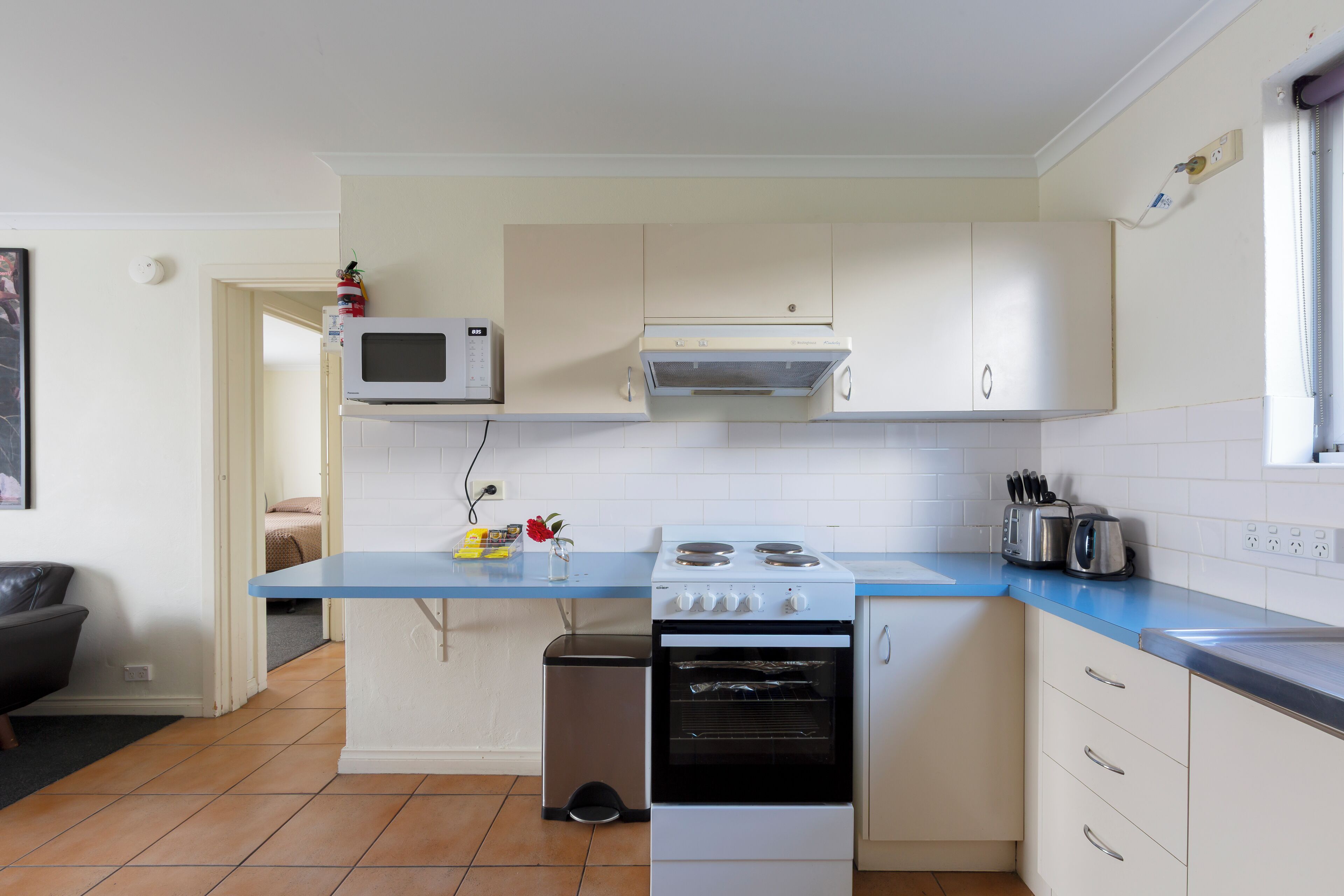A compact kitchen with a stove, microwave, and a small trash bin.