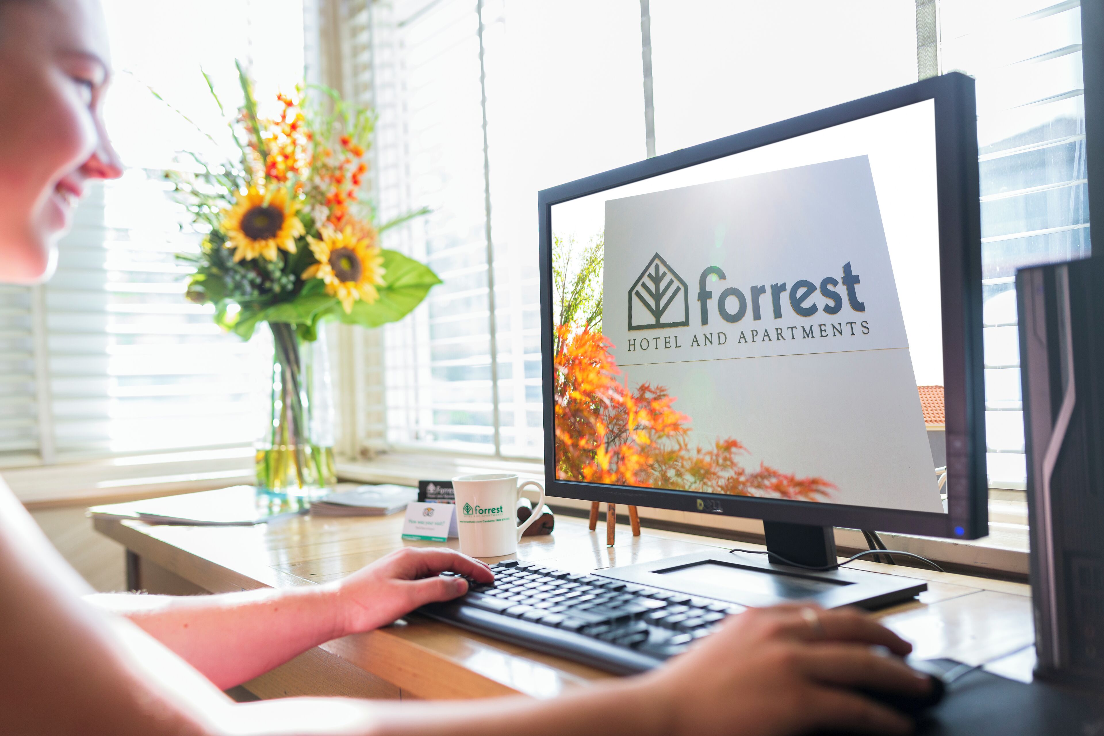 A person using a computer with a screen displaying the logo of 'Forrest Hotel and Apartments'.