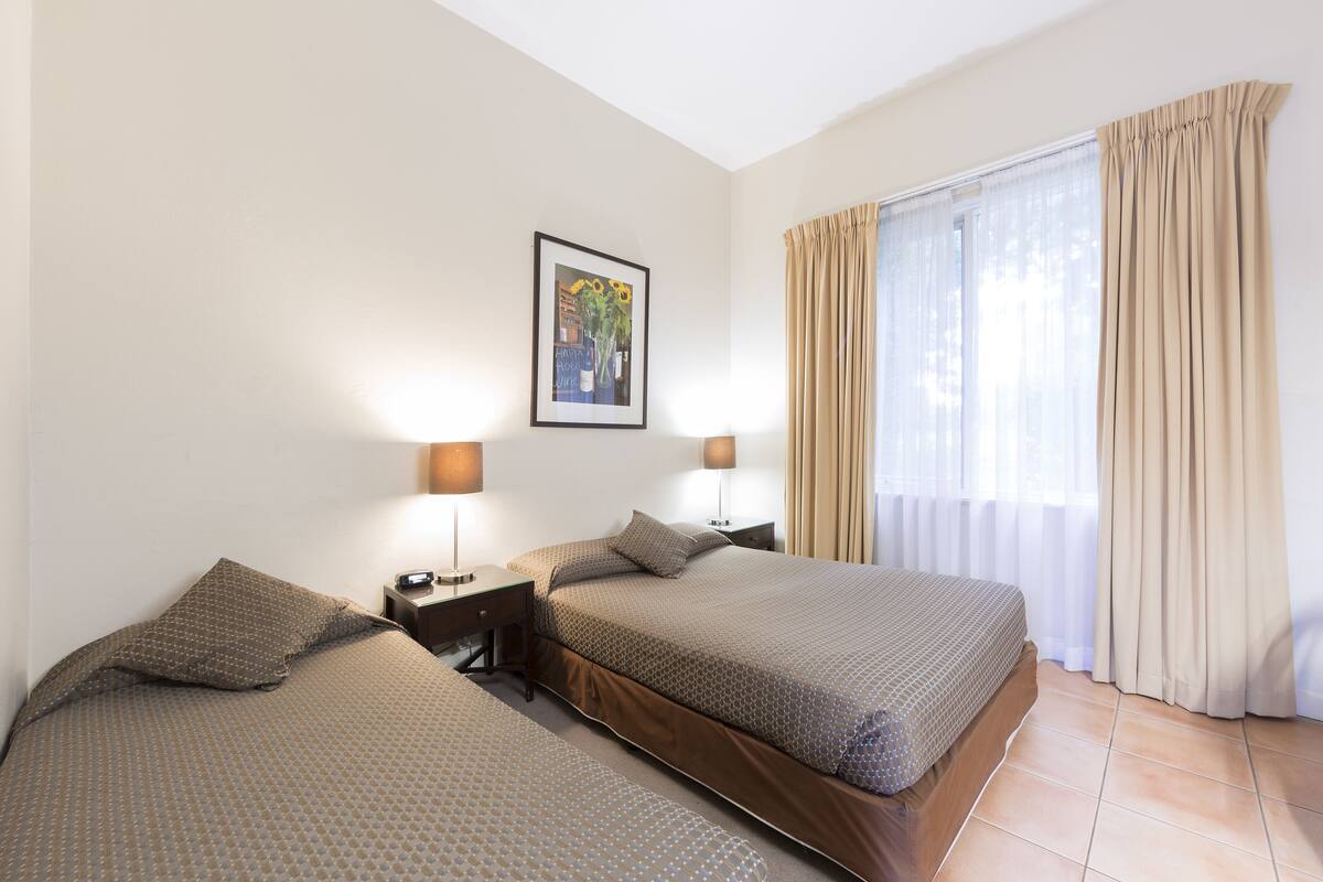 A hotel room with two beds, a framed picture on the wall, and a window with curtains.