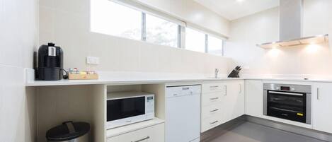 A modern kitchen with white cabinets, a dishwasher, an oven, and a microwave.