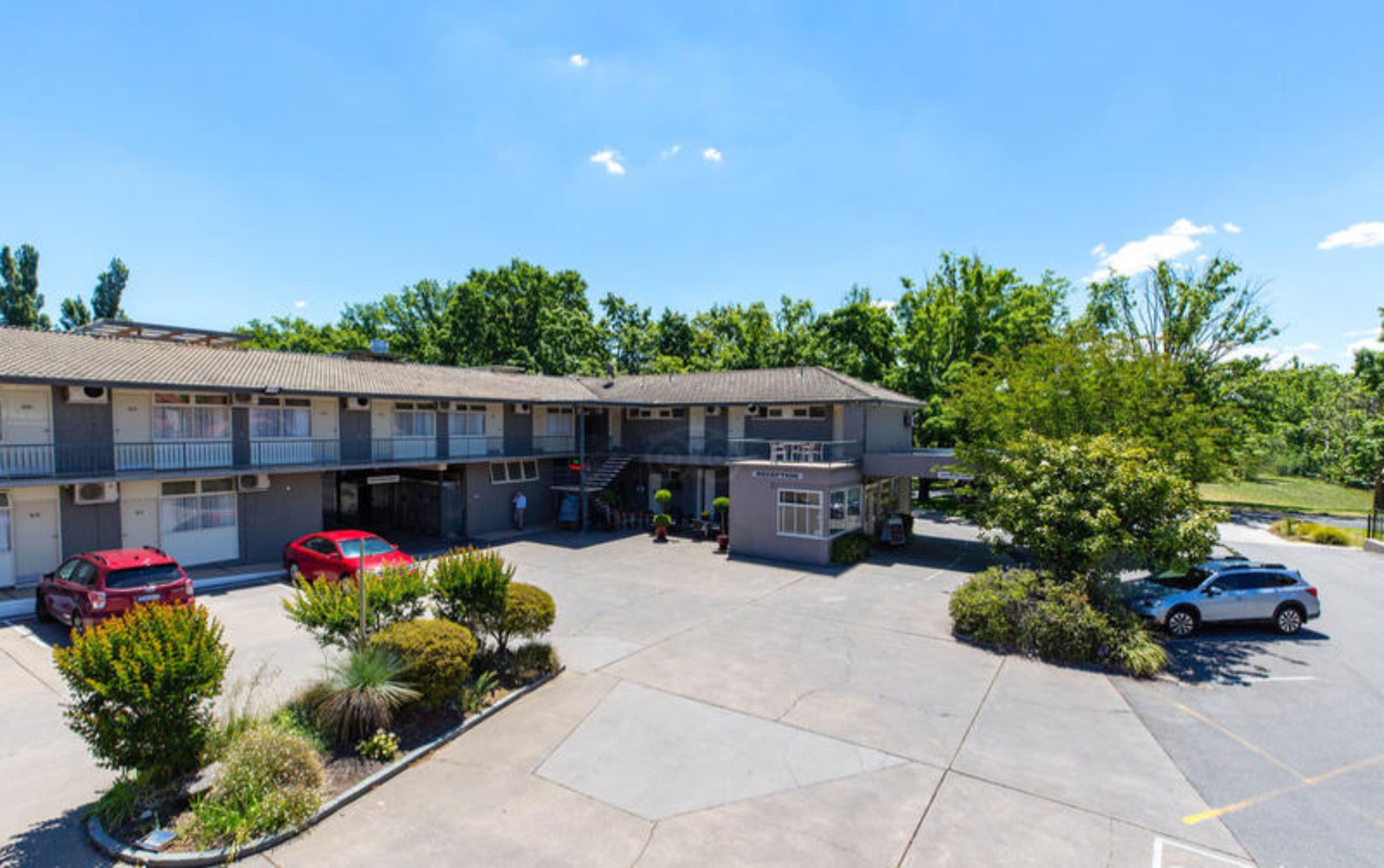 A two-story motel with a parking lot, a covered outdoor seating area, and a small garden.