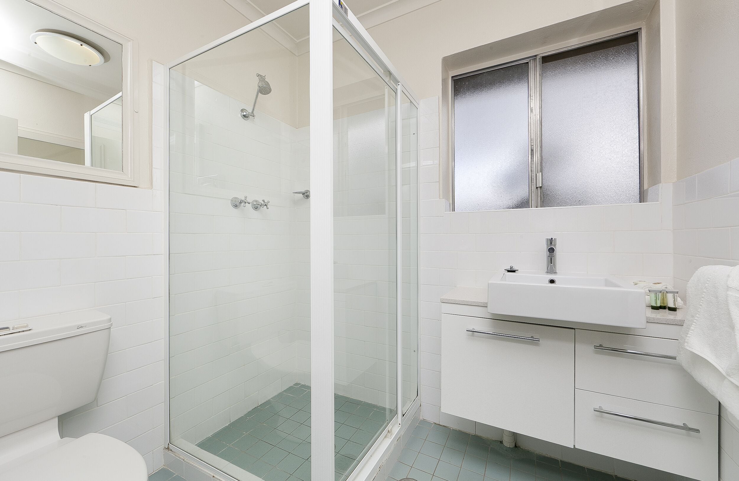 Un baño moderno con ducha envuelta en vidrio, un lavabo blanco y un espejo sobre él.