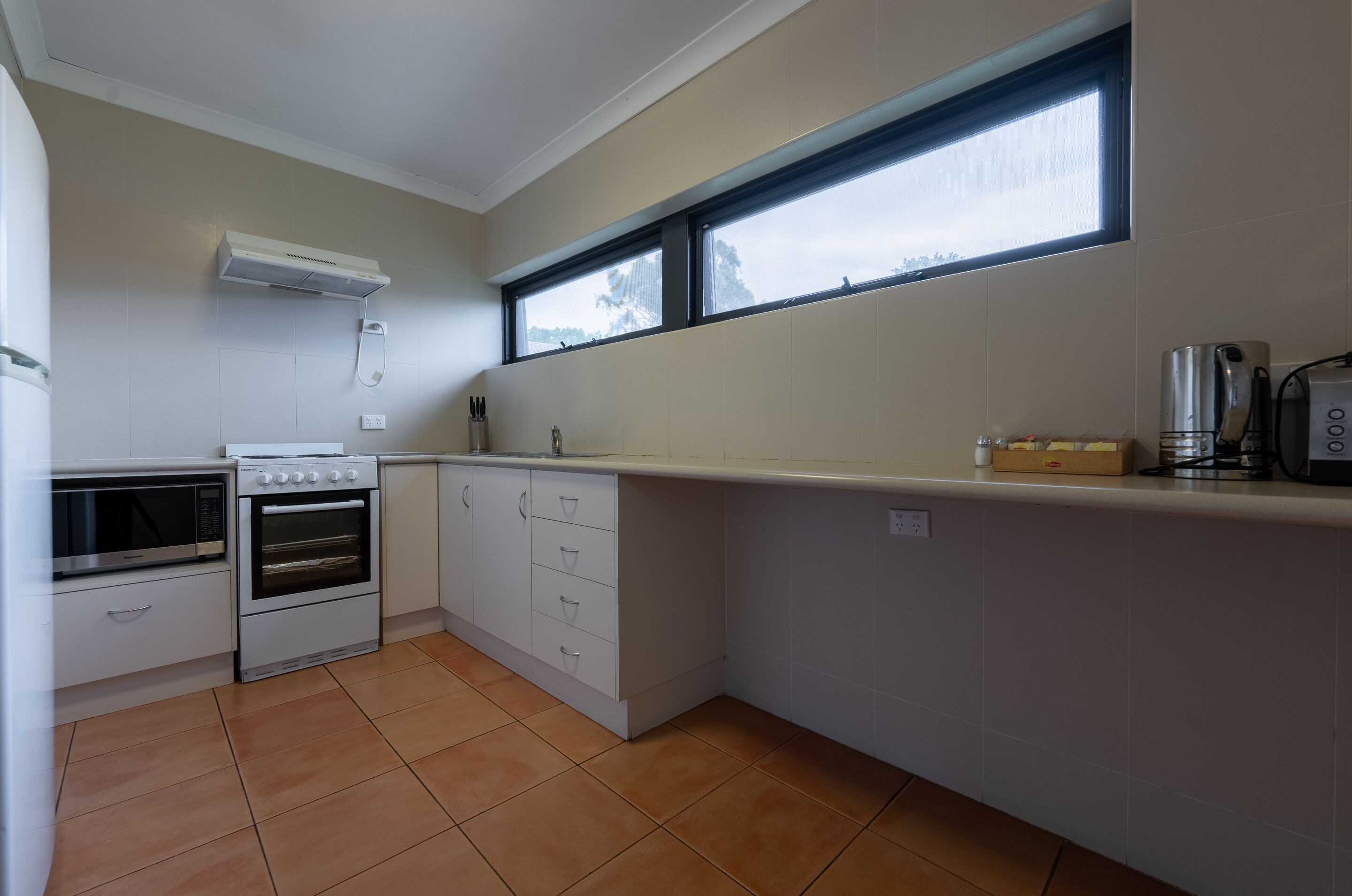 A kitchen with white cabinets, a built-in oven, a microwave, and a window above the counter.