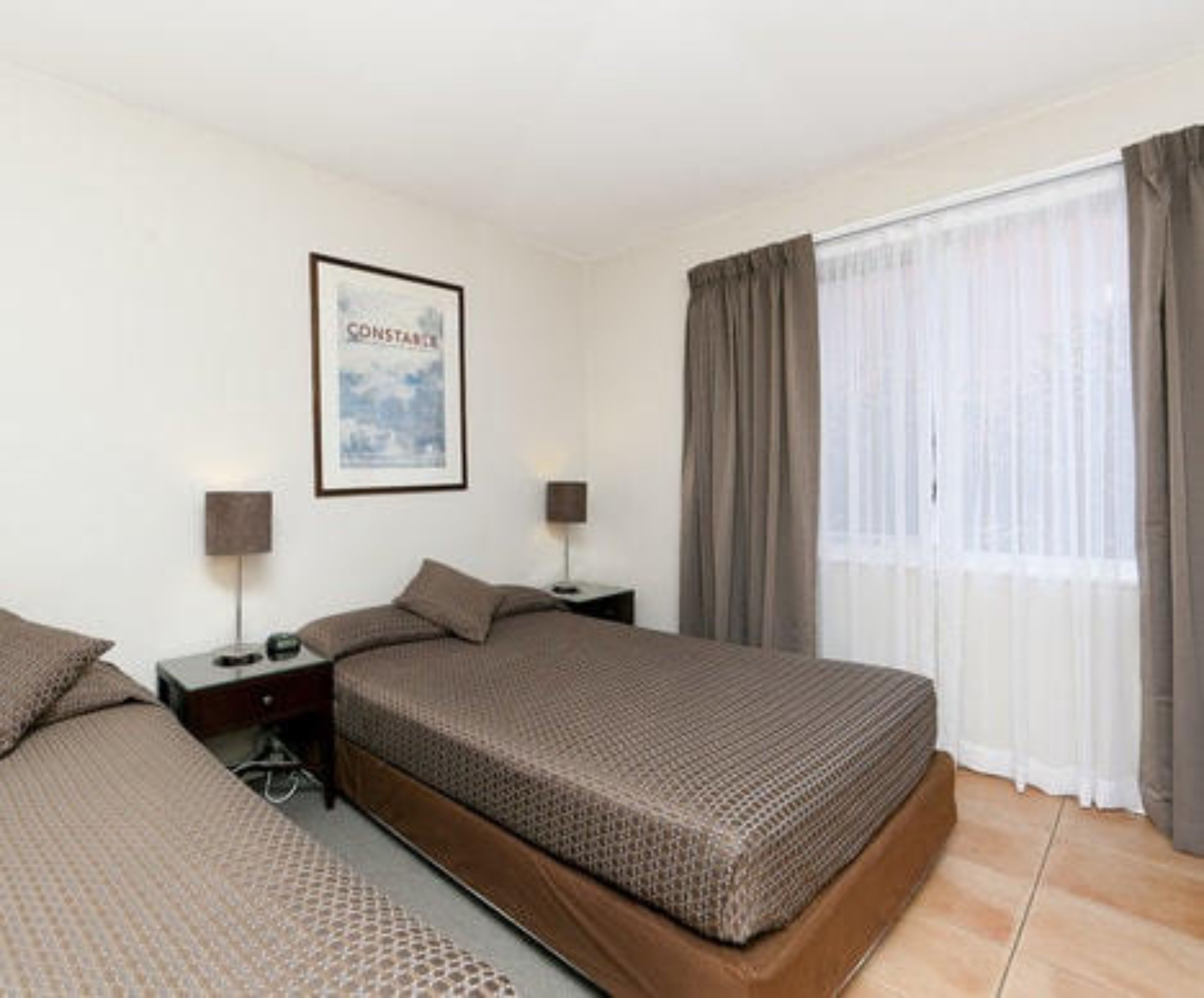 Habitació d'hotel amb dos llits, un quadre al mur i una finestra amb cortines.