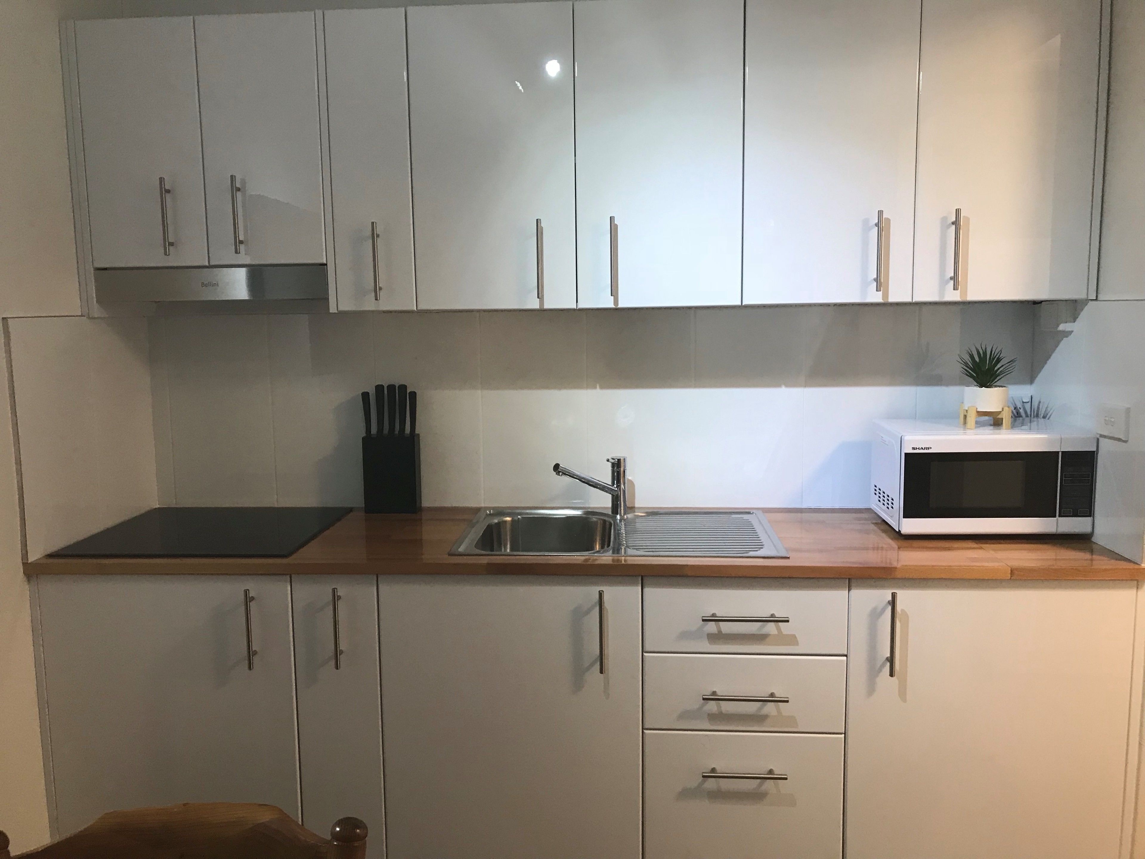 A modern kitchen with white cabinets, a stainless steel sink, a microwave, and a knife block.
