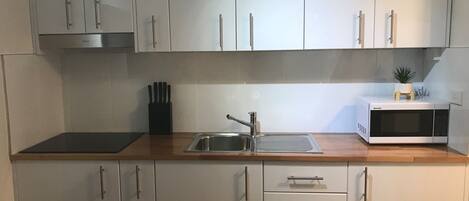 A modern kitchen with white cabinets, a stainless steel sink, a microwave, and a knife block.