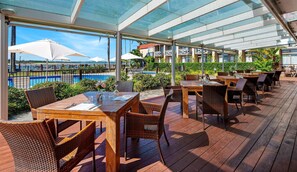 An outdoor dining area with tables and chairs, a pool, and a view of the ocean. - Comfort Resort Waters Edge (Port Macquarie)