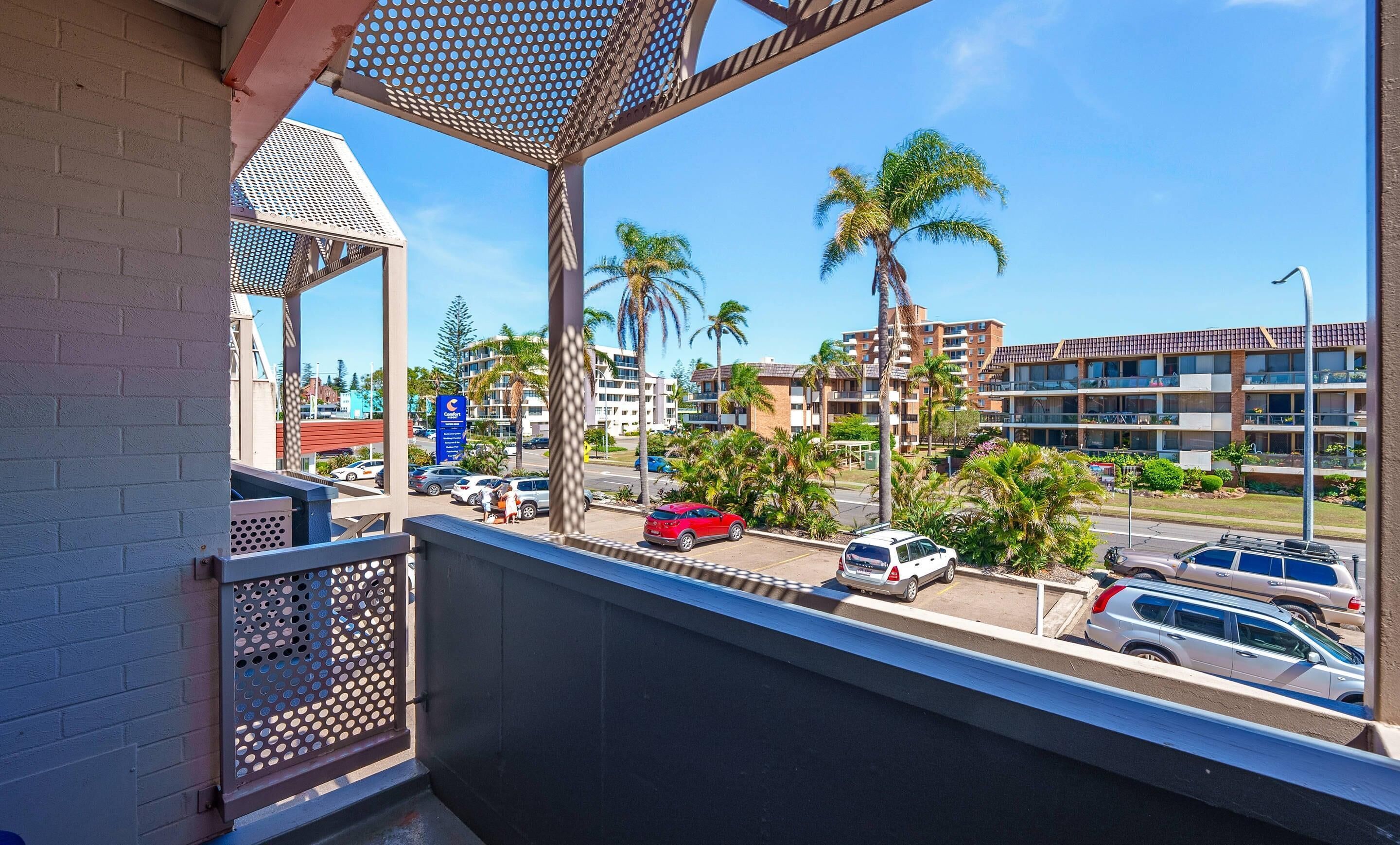 A balcony with a view of a street, palm trees, and multi-story buildings.