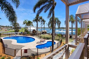 A swimming pool with a curved design, surrounded by palm trees and a view of the sea. - Comfort Resort Waters Edge (Port Macquarie)