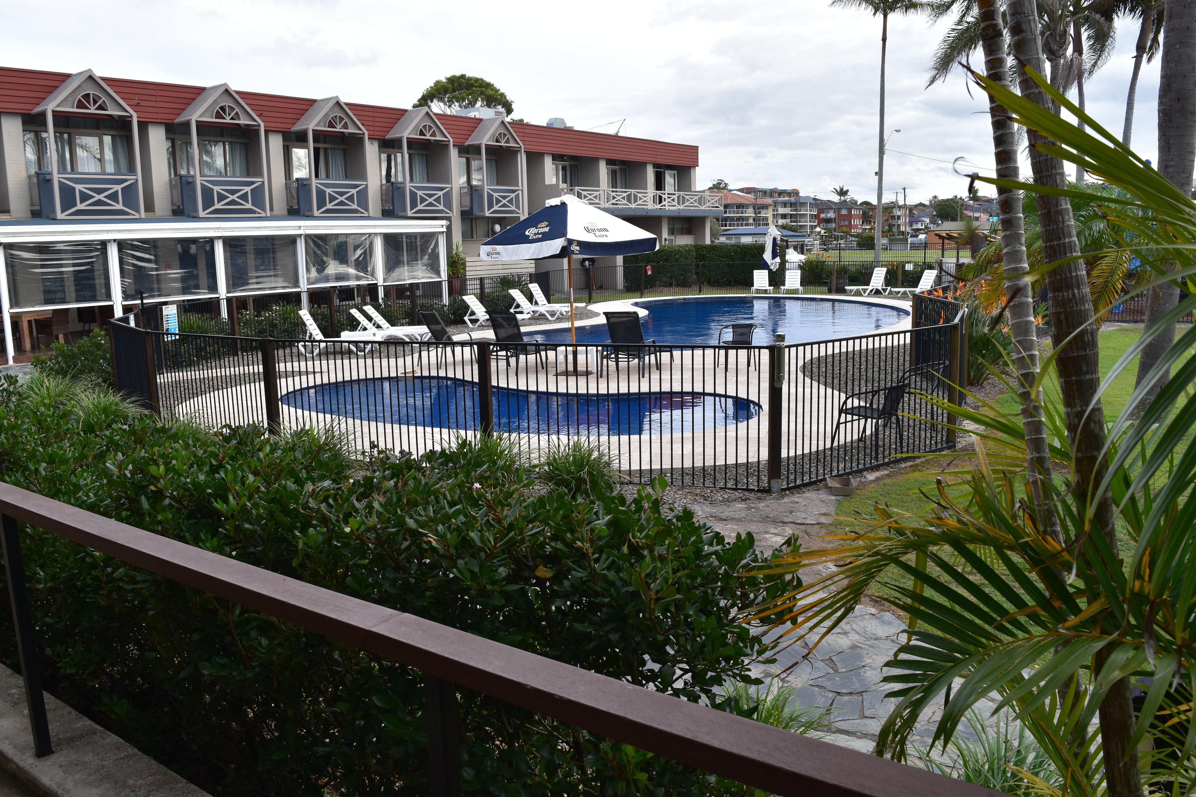 A swimming pool with lounge chairs and umbrellas, surrounded by a fence.