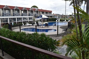 A swimming pool with lounge chairs and umbrellas, surrounded by a fence. - Comfort Resort Waters Edge (Port Macquarie)
