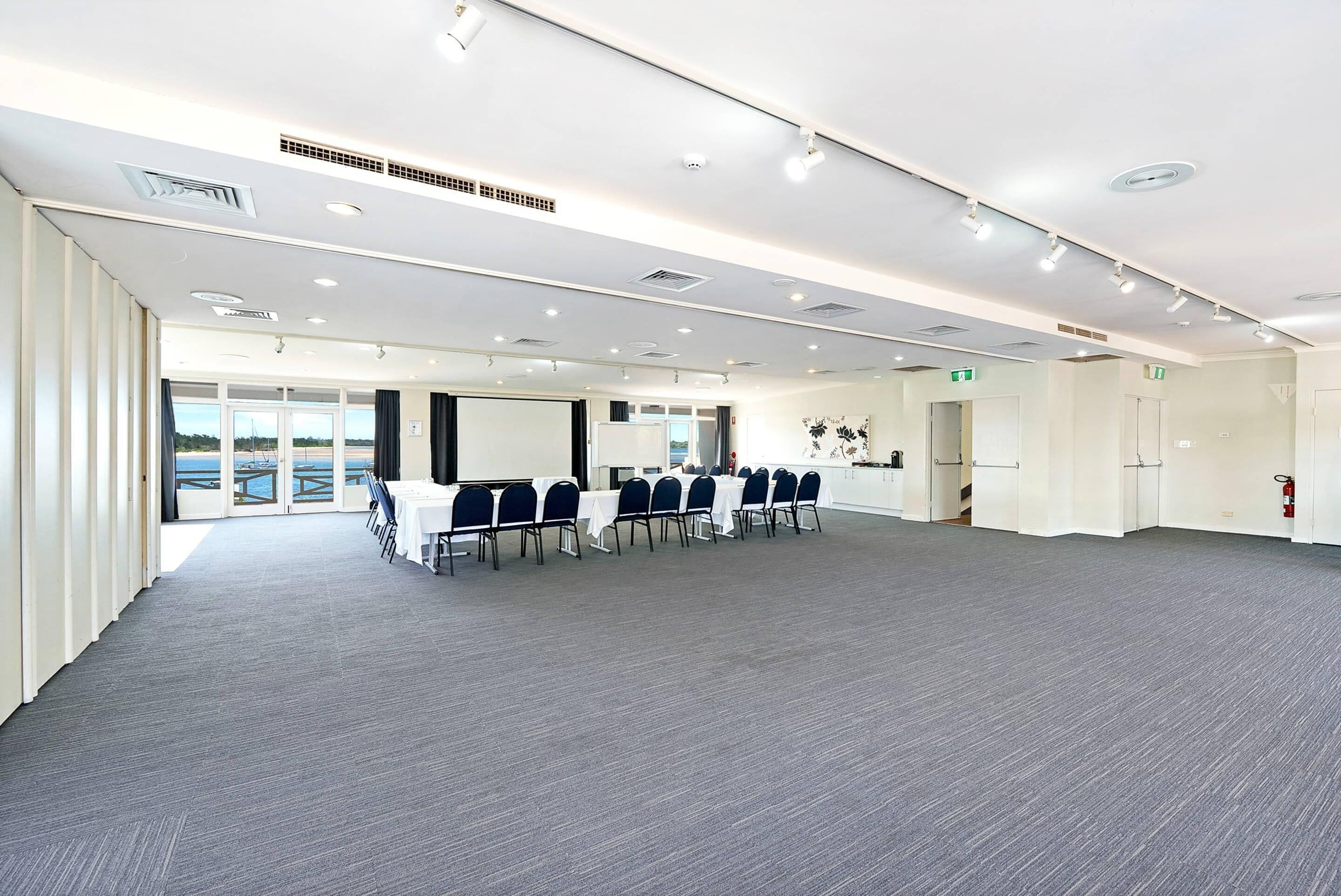 A conference room with a long table, chairs, and a large screen.