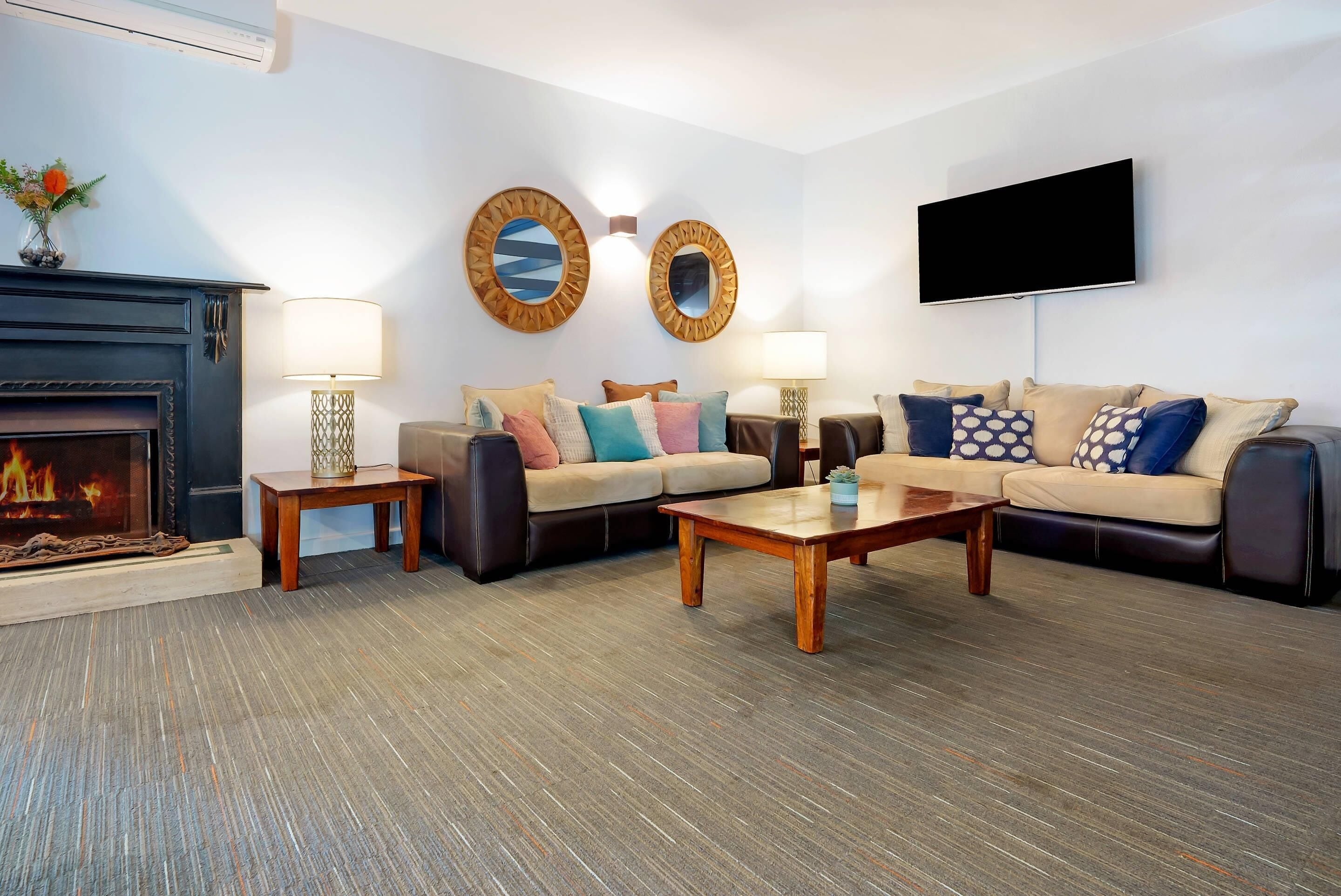 A living room with a fireplace, two sofas, a coffee table, and a TV mounted on the wall.