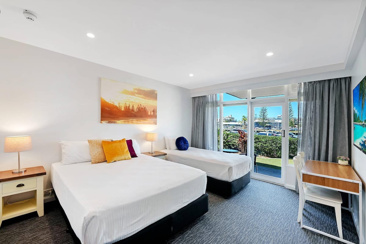 A hotel room with two beds, a desk, a chair, a window with curtains, and a painting on the wall.