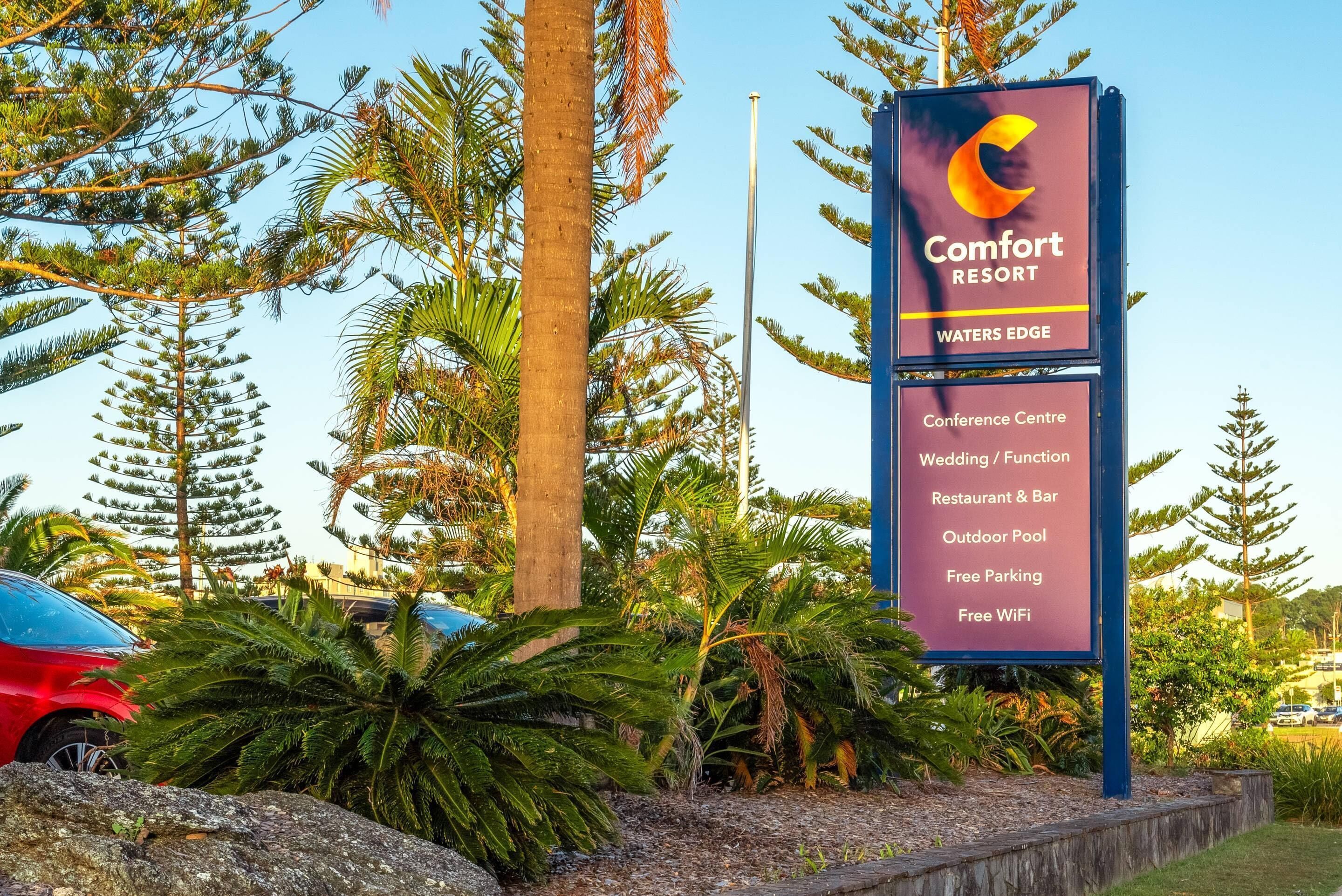 Señal de Comfort Resort Waters Edge que enumera servicios como centro de conferencias, espacio para bodas, restaurante y bar, piscina al aire libre, estacionamiento gratuito y WiFi gratuito.