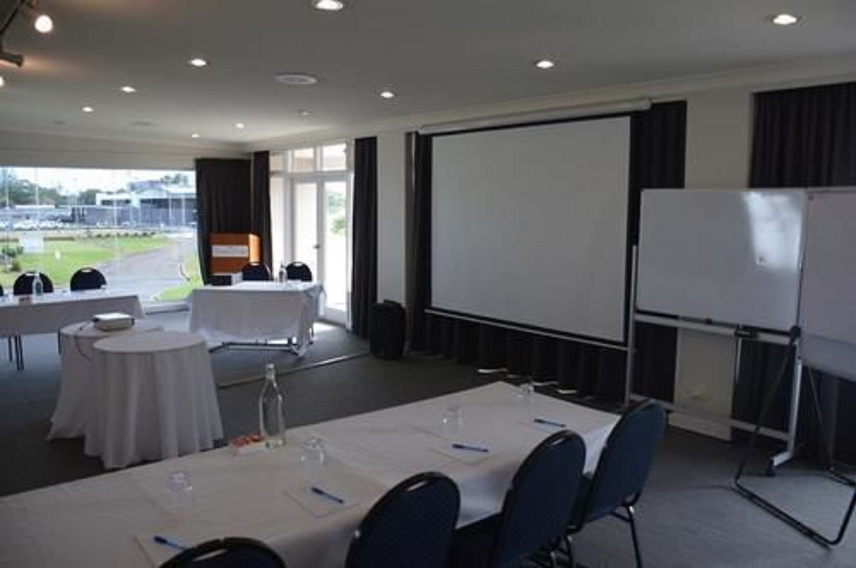 A conference room with a large screen, whiteboard, and round tables with chairs.