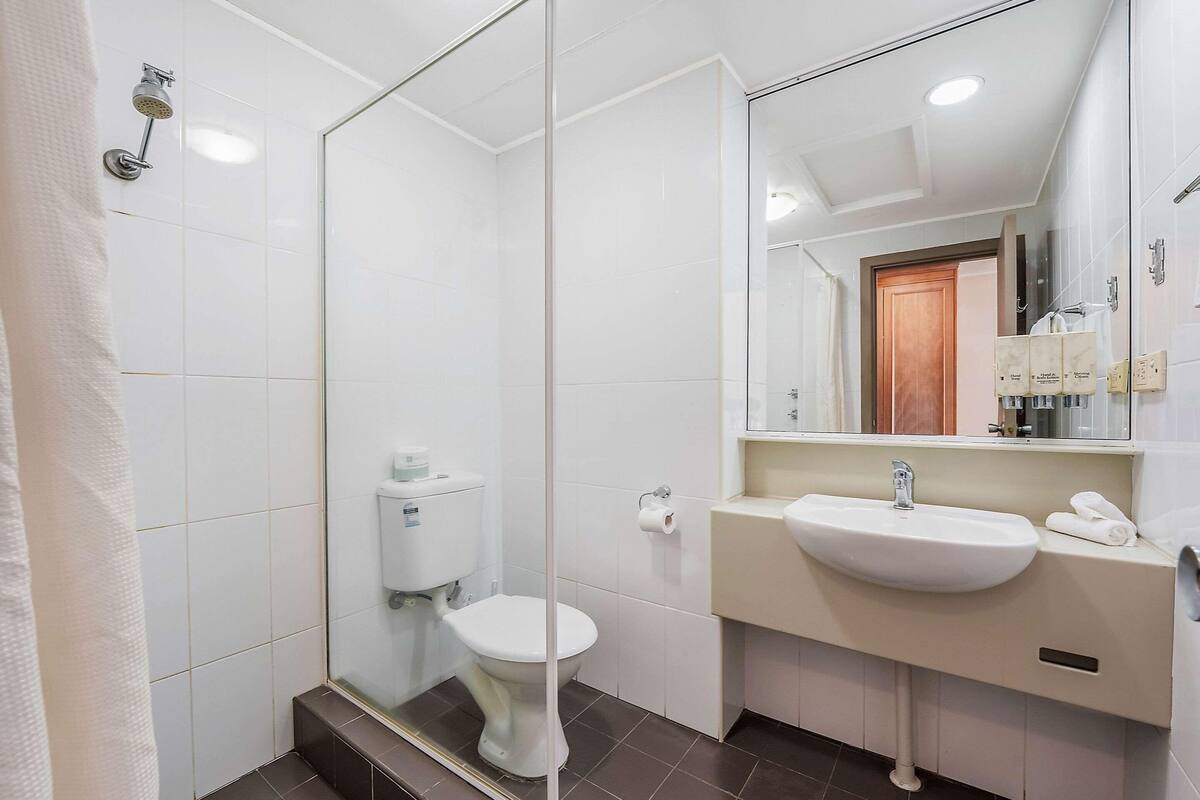 A bathroom with a glass shower enclosure, a toilet, a sink, and a mirror.
