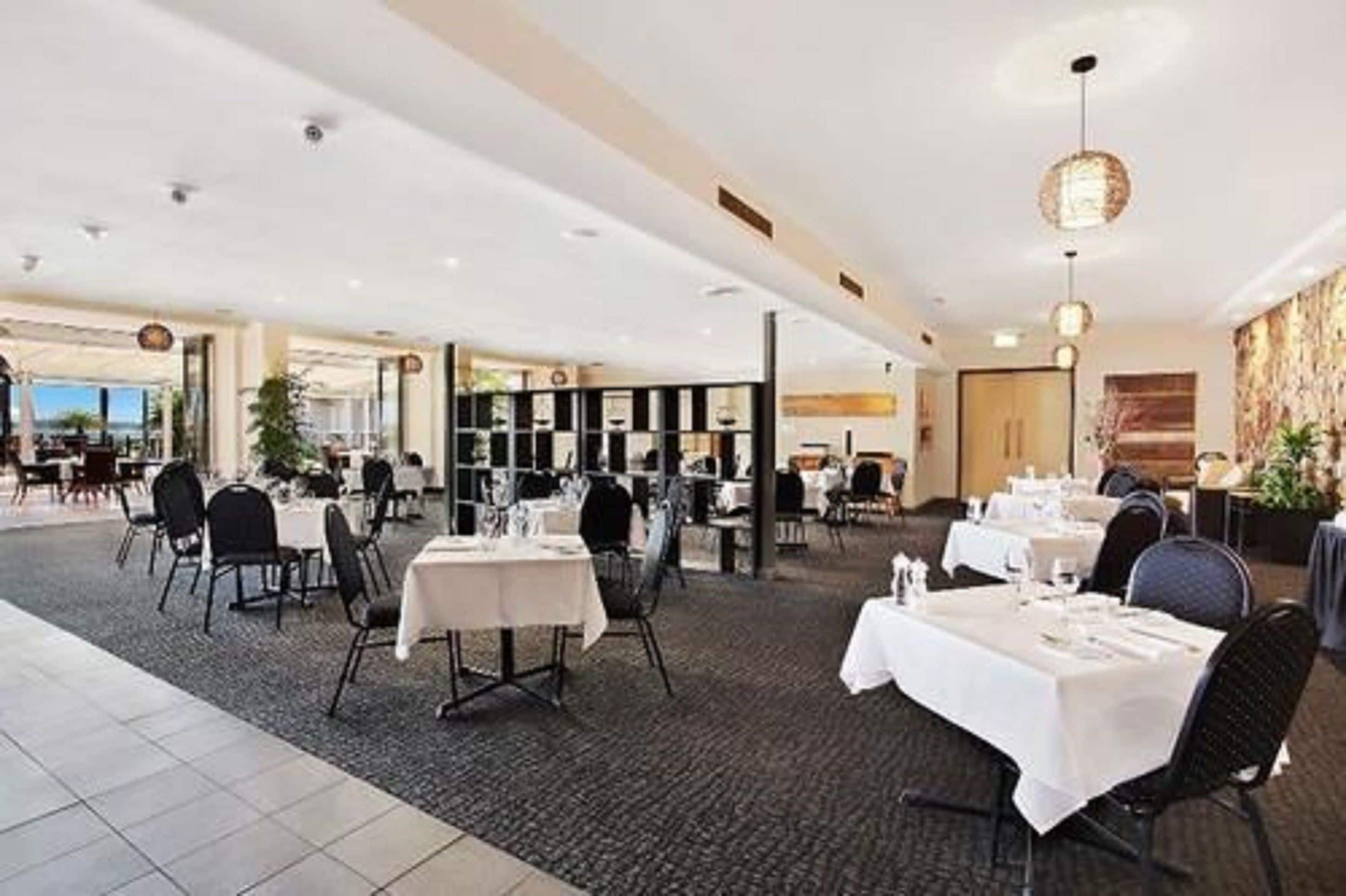 Un restaurante espacioso con varias mesas y sillas, un techo alto con iluminación empotrada y vistas al exterior.