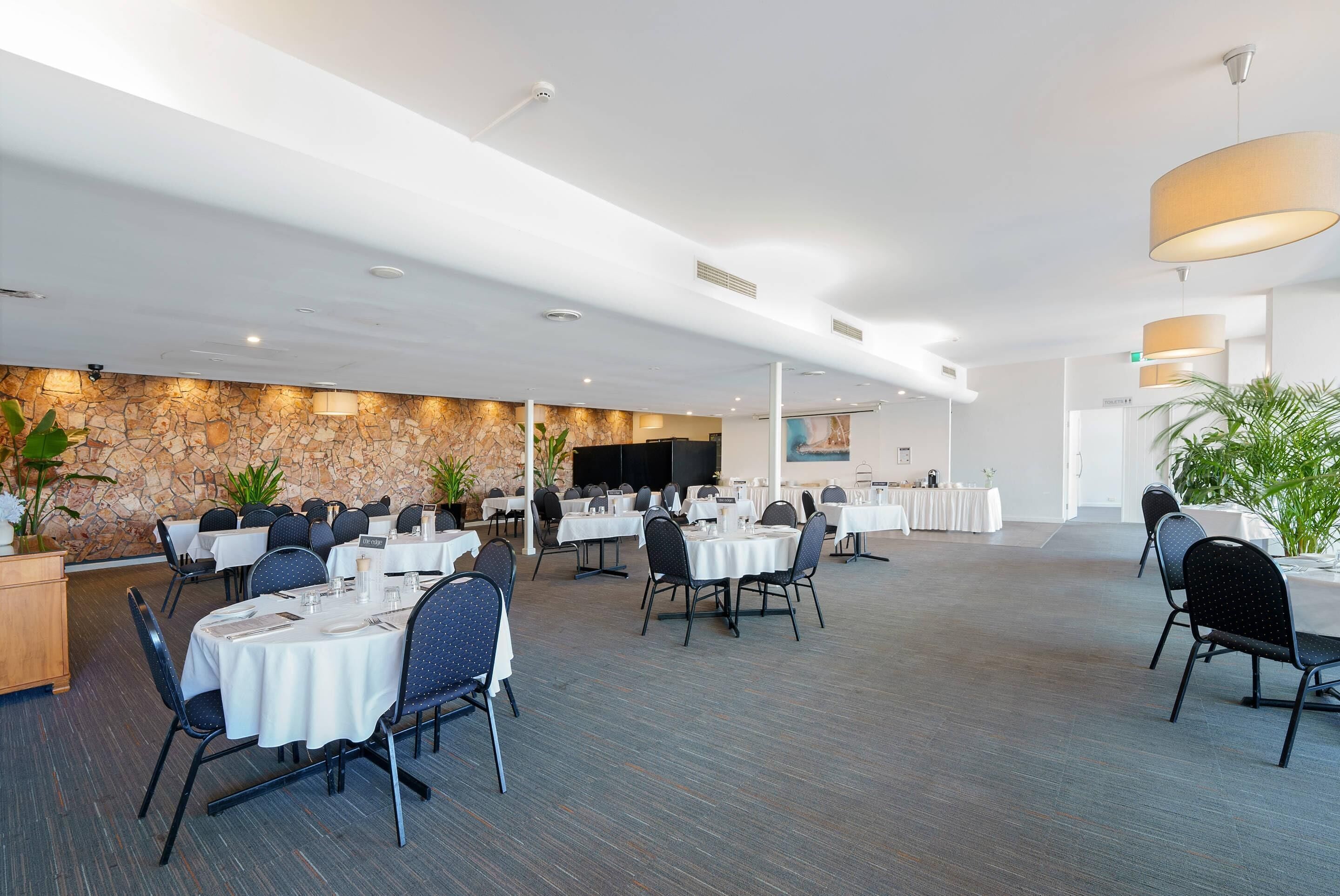 A spacious conference room with round tables, chairs, and a stage area.