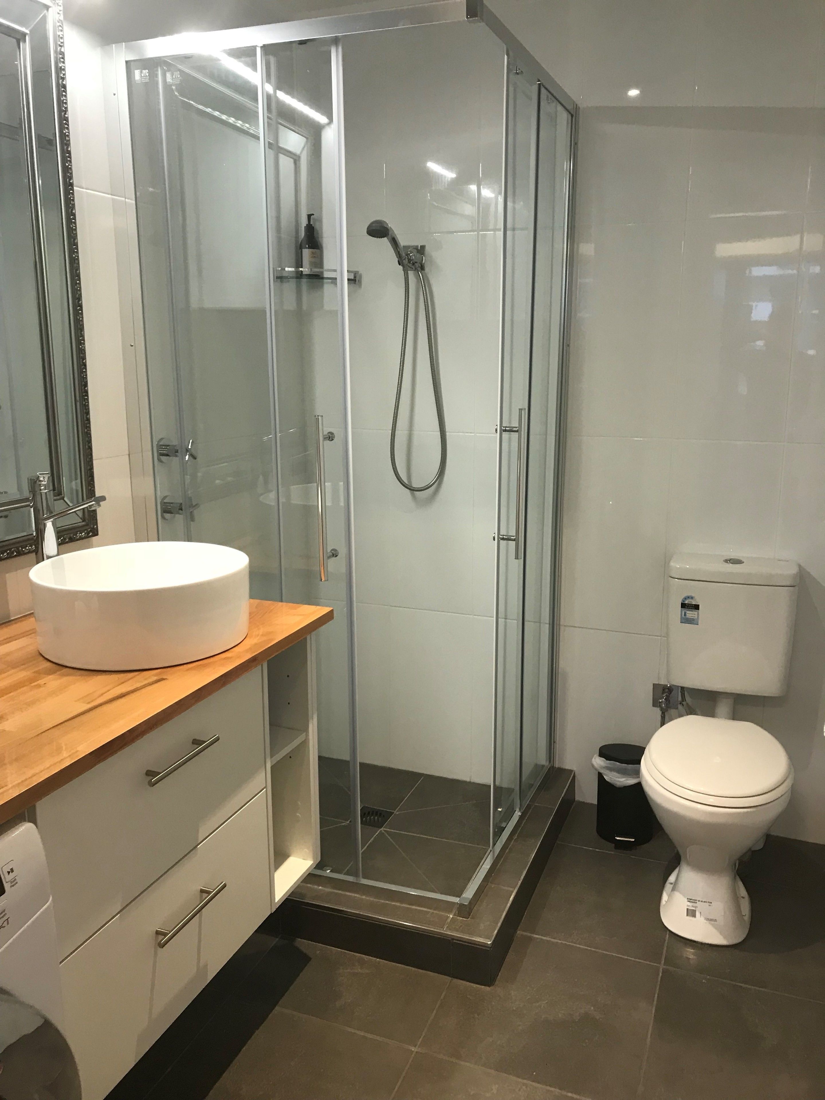 Un bany modern amb plat de dutxa tancat amb vidre, un lavabo blanc i un vàter.
