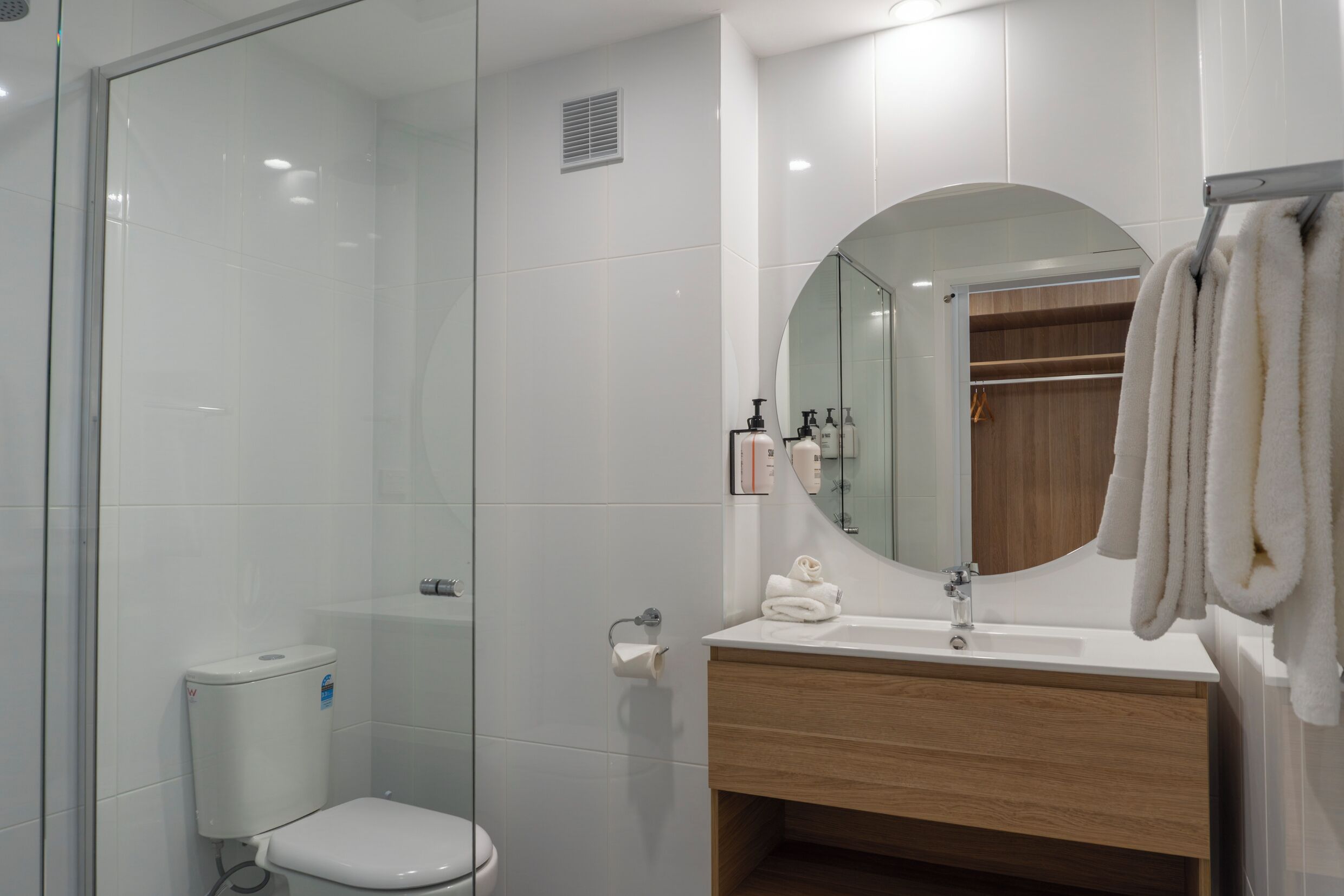 A modern bathroom with a glass shower enclosure, a toilet, a sink with a mirror, and a towel rack.