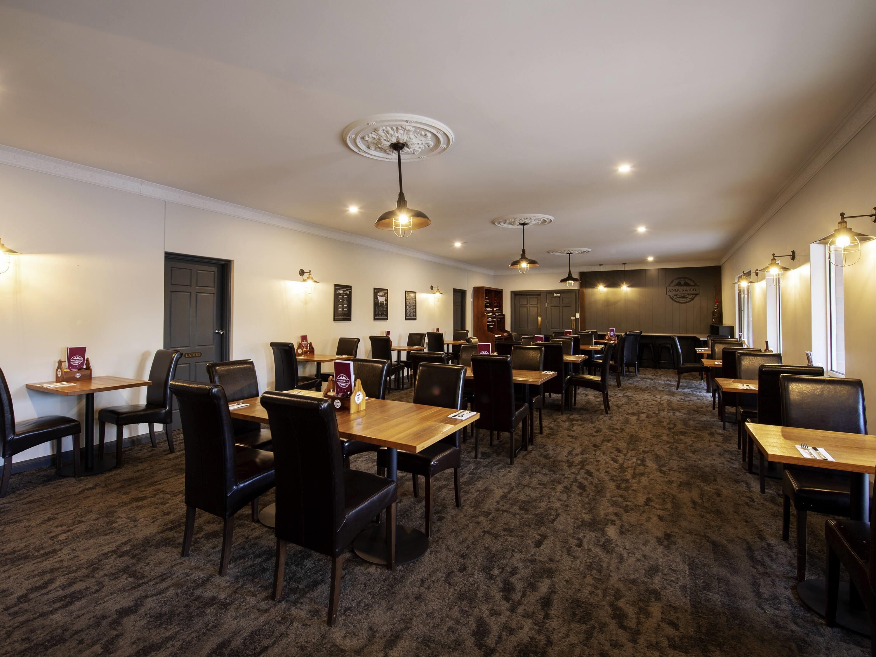 A restaurant with multiple tables and chairs, ceiling lights, and a carpeted floor.